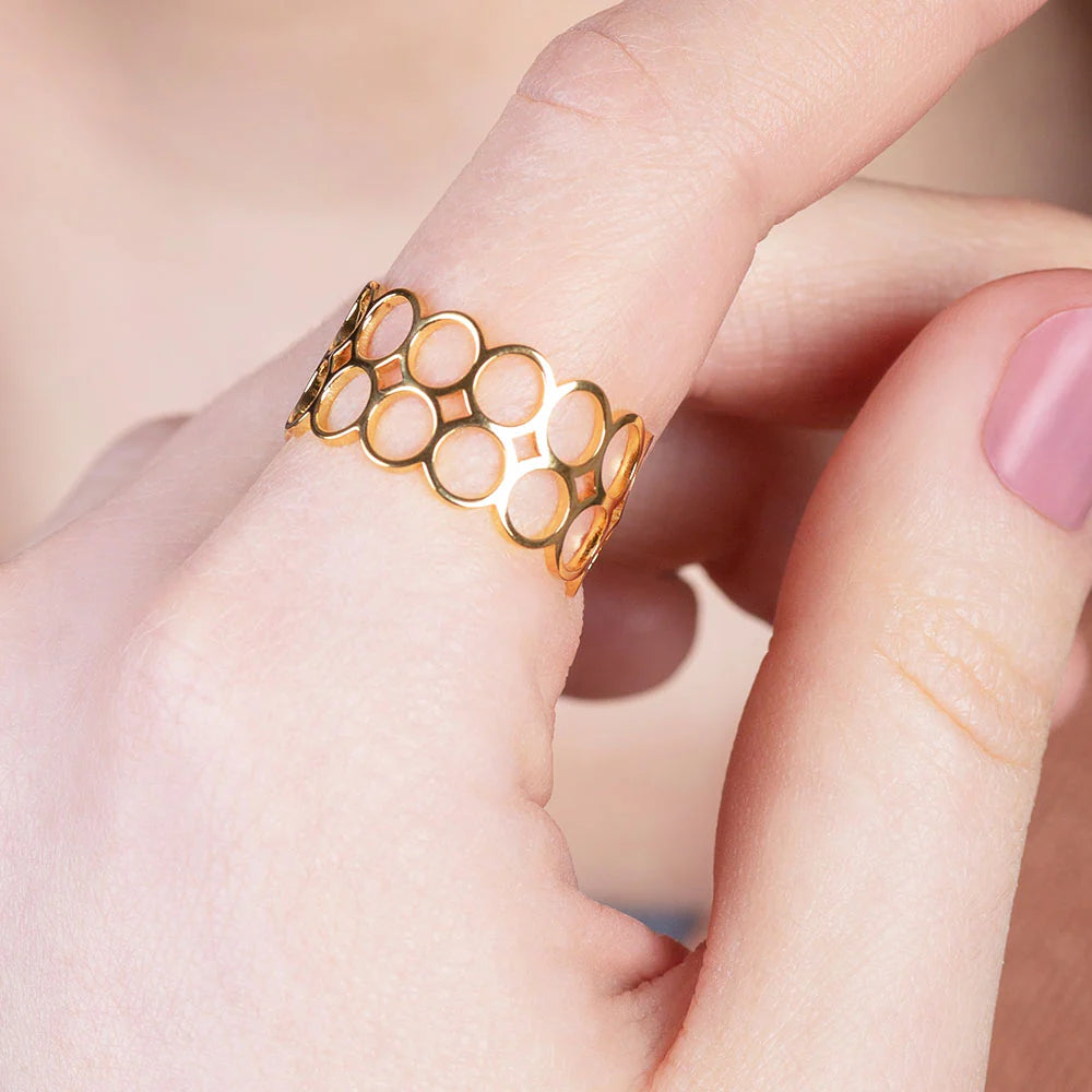 Nahaufnahme einer hellhäutigen Hand, die einen goldenen Ring mit Wabenmuster am Mittelfinger trägt. Die Fingernägel sind sauber getrimmt und hellrosa lackiert.