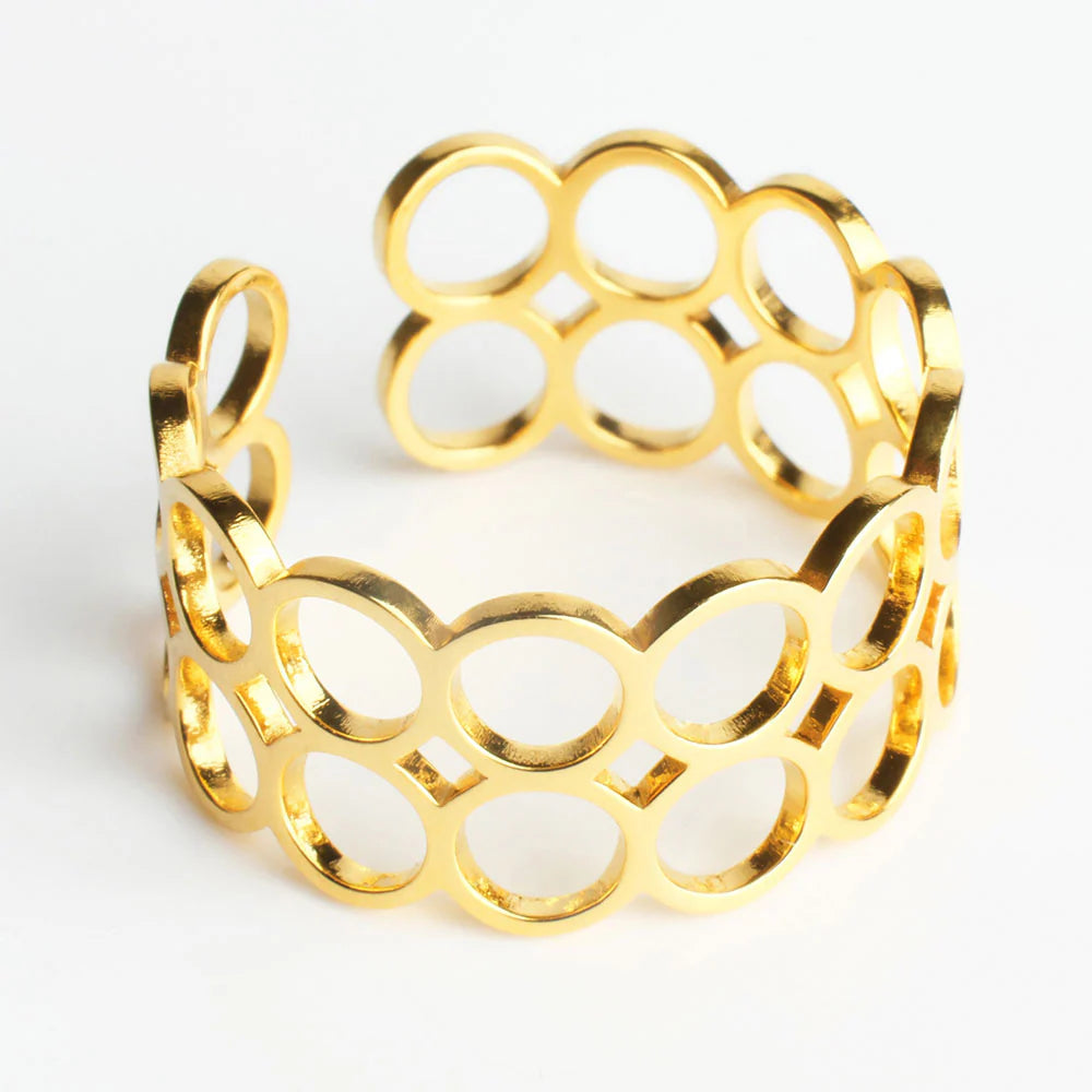 Ein Goldring mit offenem Band, in dem ovale und runde Formen ineinandergreifen und ein geometrisches Muster bilden. Der Ring hat eine glänzende, polierte Oberfläche.