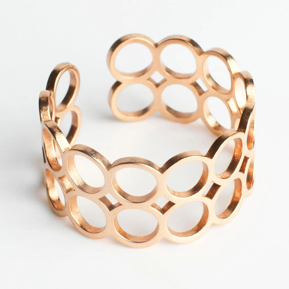 Ein goldenes Manschettenarmband mit einem durchbrochenen Muster aus ineinandergreifenden ovalen Formen auf weißem Hintergrund.