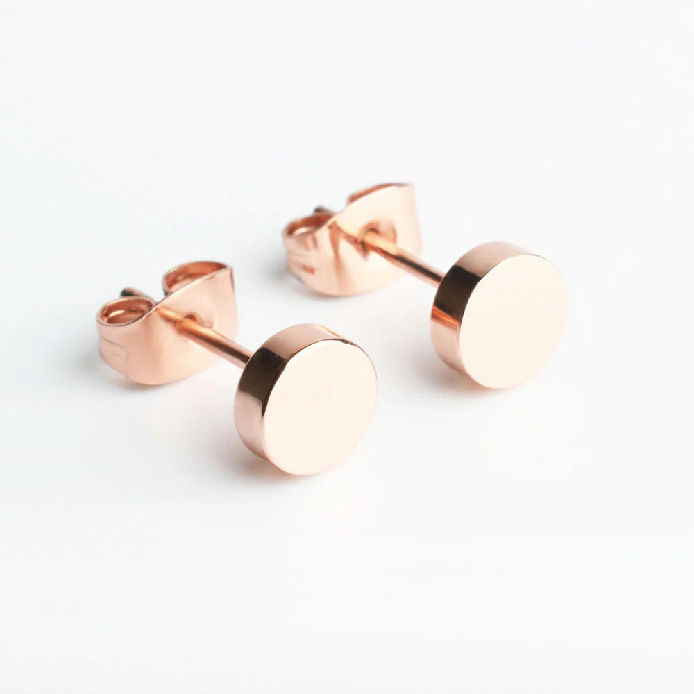 Ein Paar schlichte, runde Ohrstecker aus Roségold mit glänzender, polierter Oberfläche, die auf weißem Hintergrund präsentiert werden.