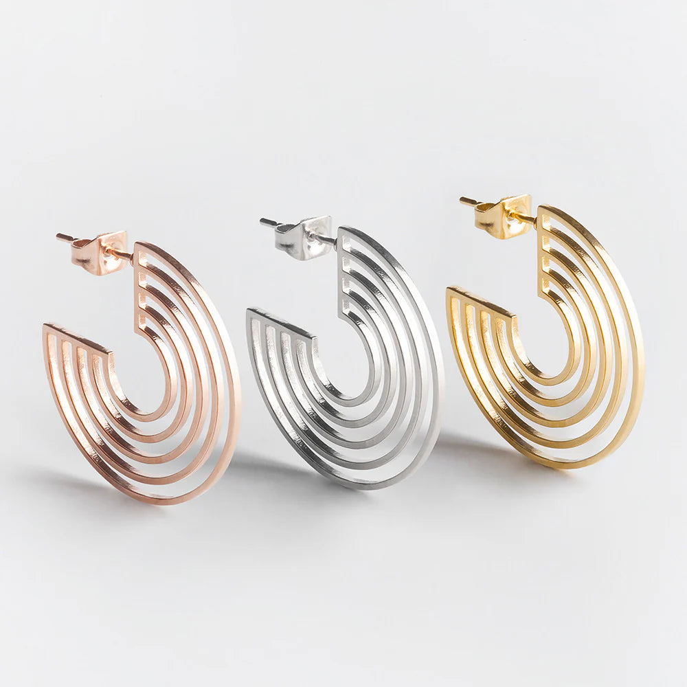 Drei metallische, halbrunde Ohrringe mit geometrischem, geschichtetem Design werden nebeneinander in Roségold, Silber und Gold auf weißem Hintergrund präsentiert.