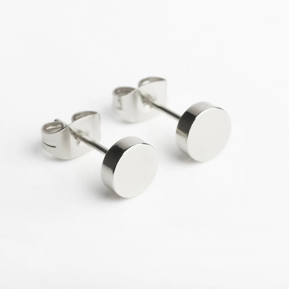 Ein Paar minimalistische silberne Ohrstecker mit flacher, runder Vorderseite und Schmetterlingsverschluss auf weißem Hintergrund.