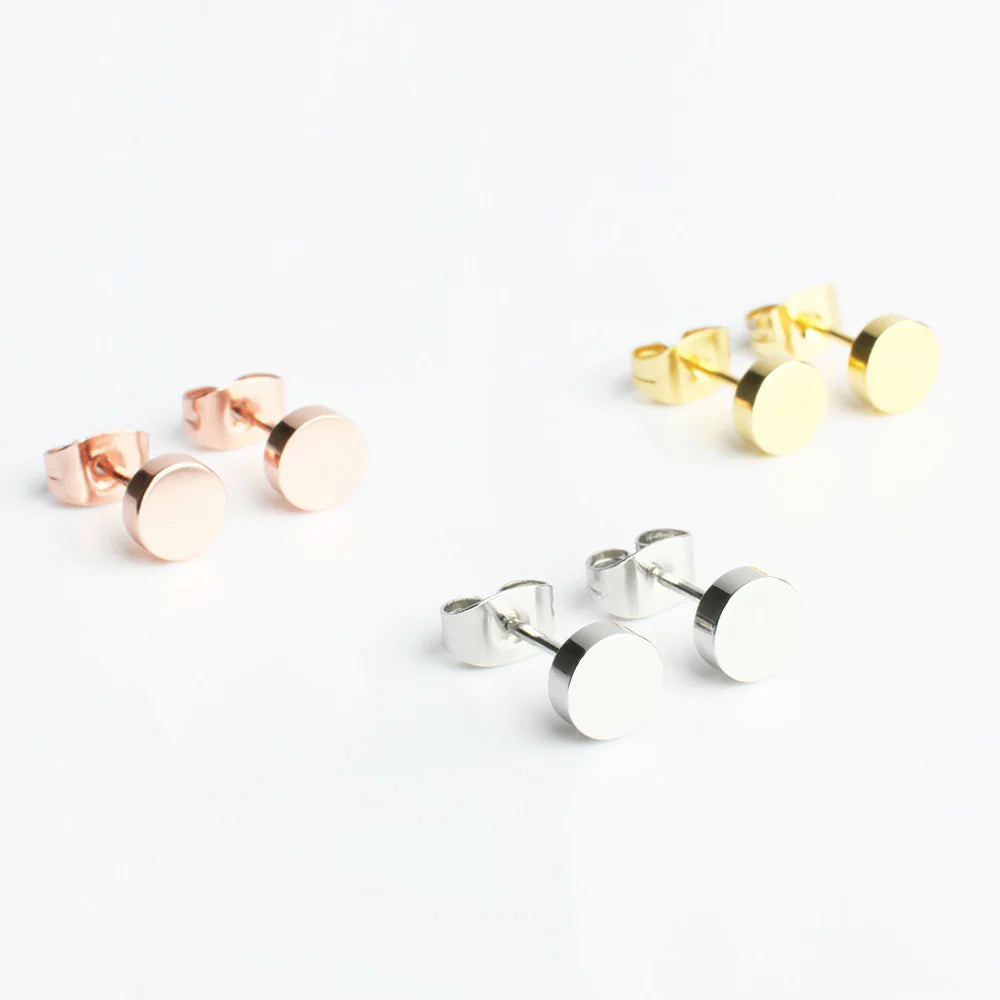 Drei Paare runder Ohrstecker in verschiedenen Metallic-Ausführungen - Roségold, Gold und Silber - sind auf einer weißen Fläche ausgestellt.