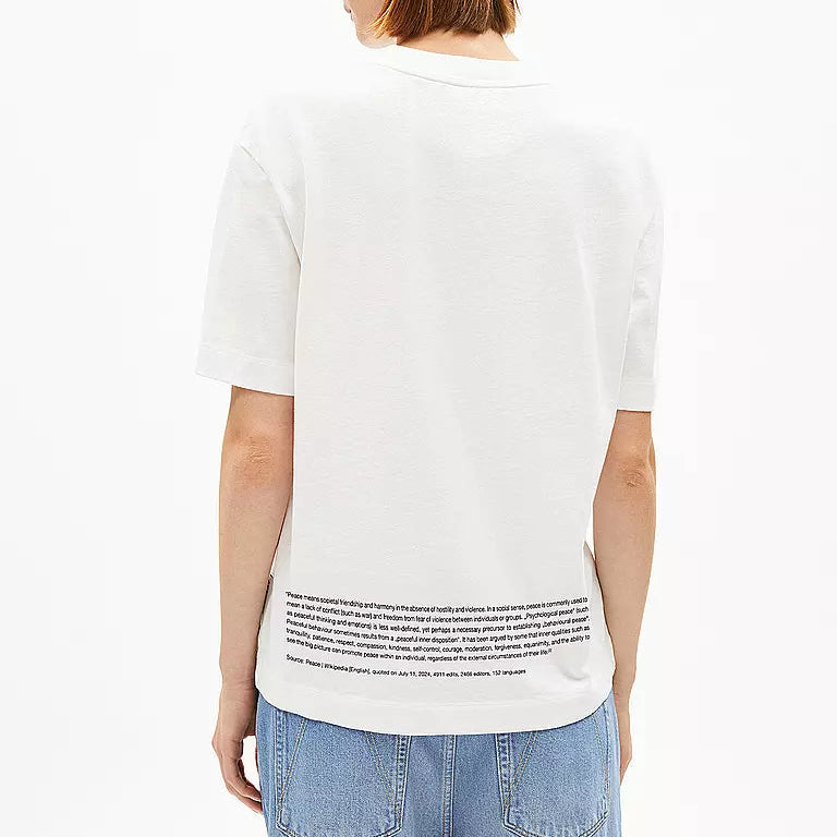 Eine Person mit kurzen Haaren, die eine blaue Kappe, ein weißes T-Shirt mit kleinem Text am Saum und hellblaue Jeans trägt, wird von hinten vor einem einfarbigen weißen Hintergrund gezeigt.