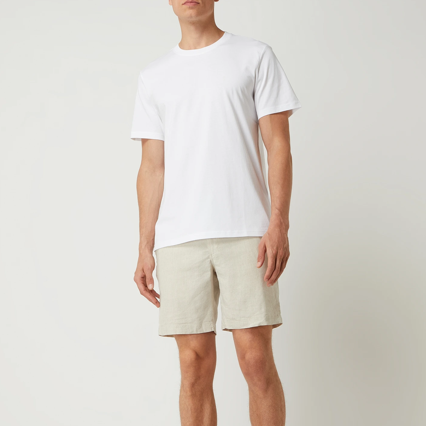 Mann trägt ein weißes T-Shirt und beige Shorts vor neutralem Hintergrund.