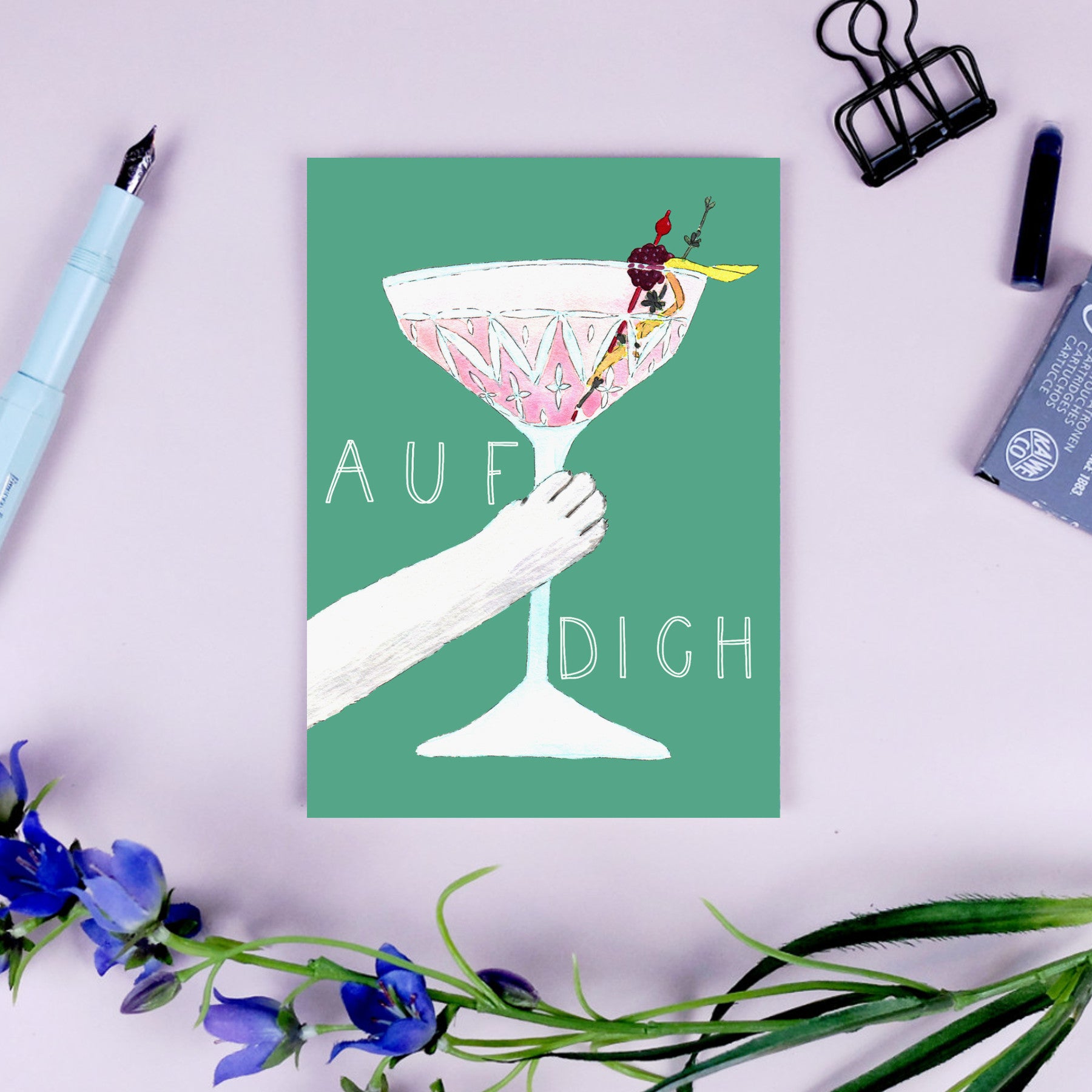 Illustration einer Hand, die ein Cocktailglas hält, mit dem Text "AUF DICH" umgeben von Büroartikeln und Blumen.
