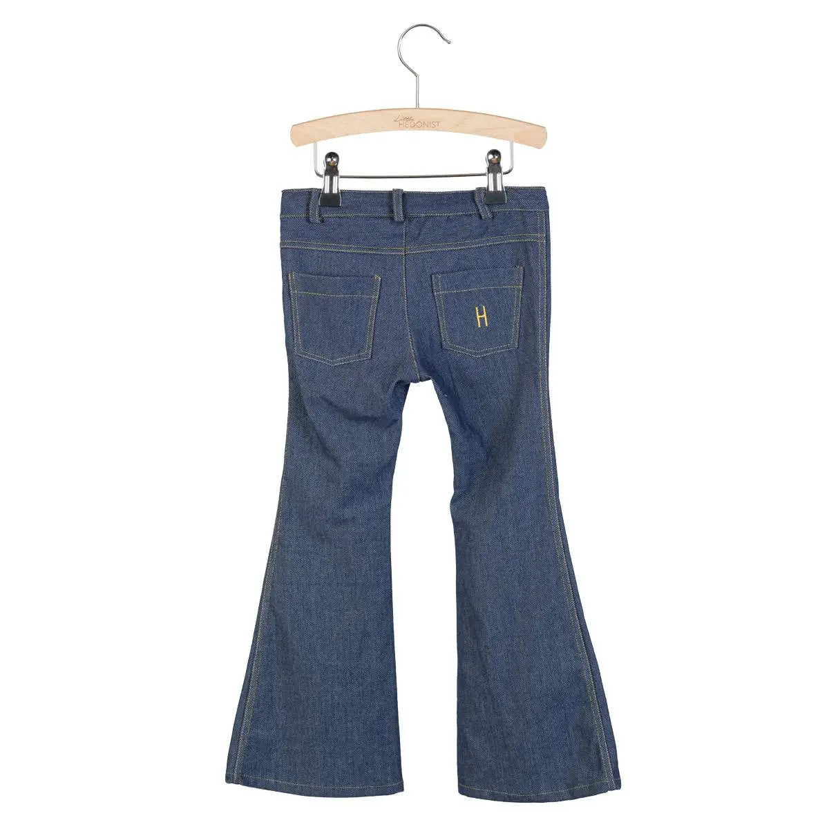 Auf einem Holzbügel hängende Kinderjeans aus blauem Jeansstoff, von hinten gesehen mit zwei Taschen und einem gelben, auf die rechte Tasche aufgenähten H.
