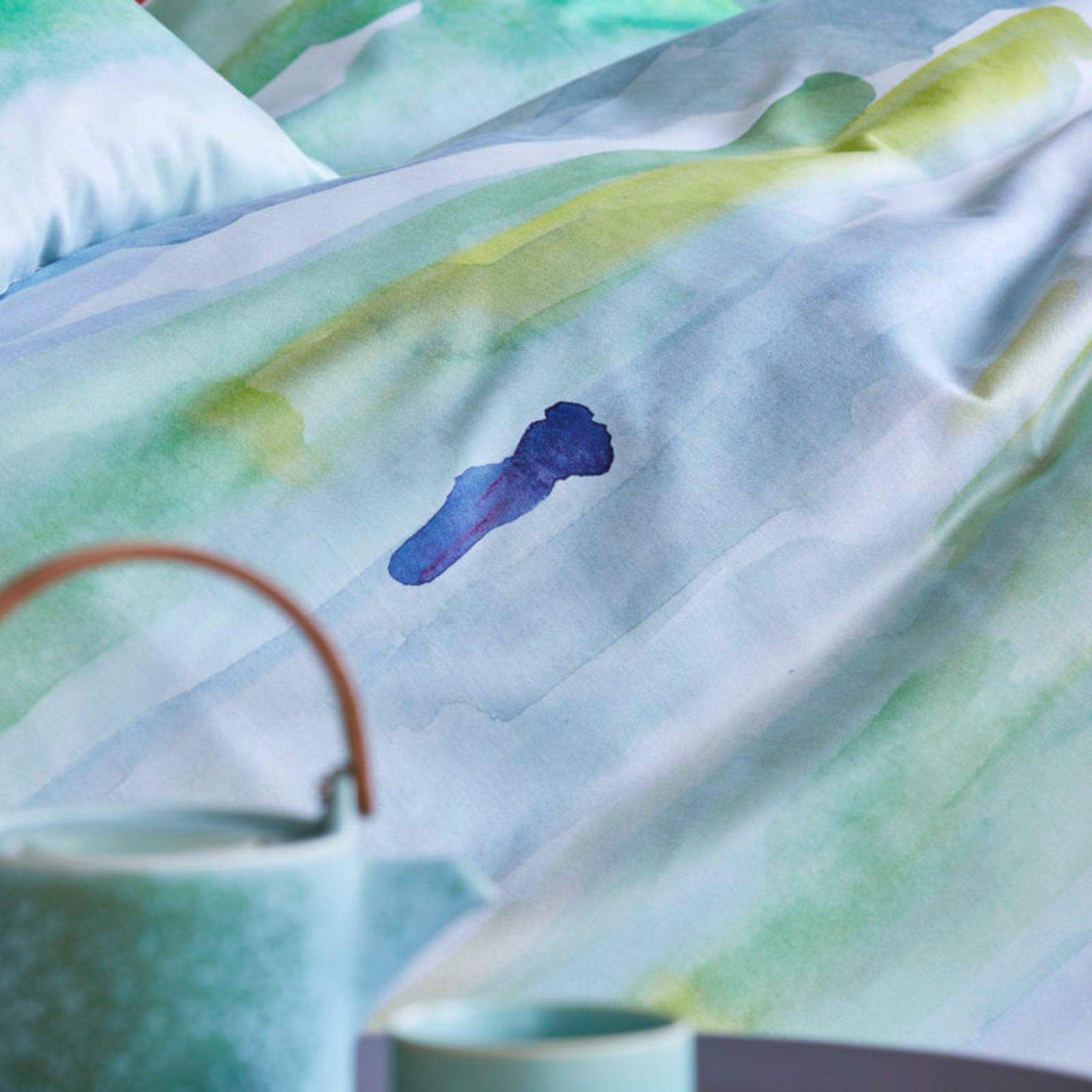 Nahaufnahme eines Betttuchs mit aquarellfarbenem Druck in Blau- und Grüntönen und einem blauen Klecks.