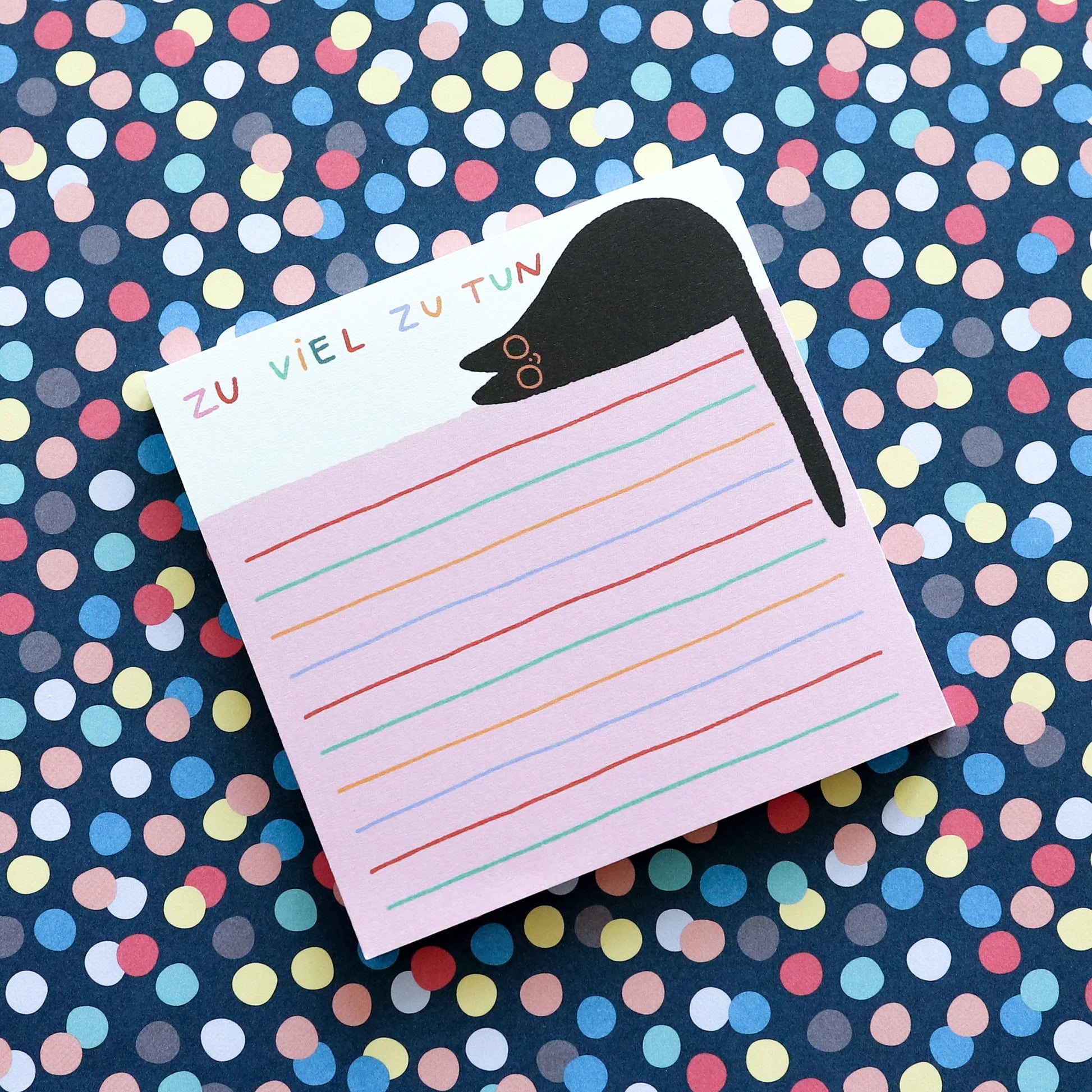 Notizblock mit der Aufschrift "Zu viel zu tun", verziert mit einem schwarzen Tier, auf buntem, gepunktetem Hintergrund.