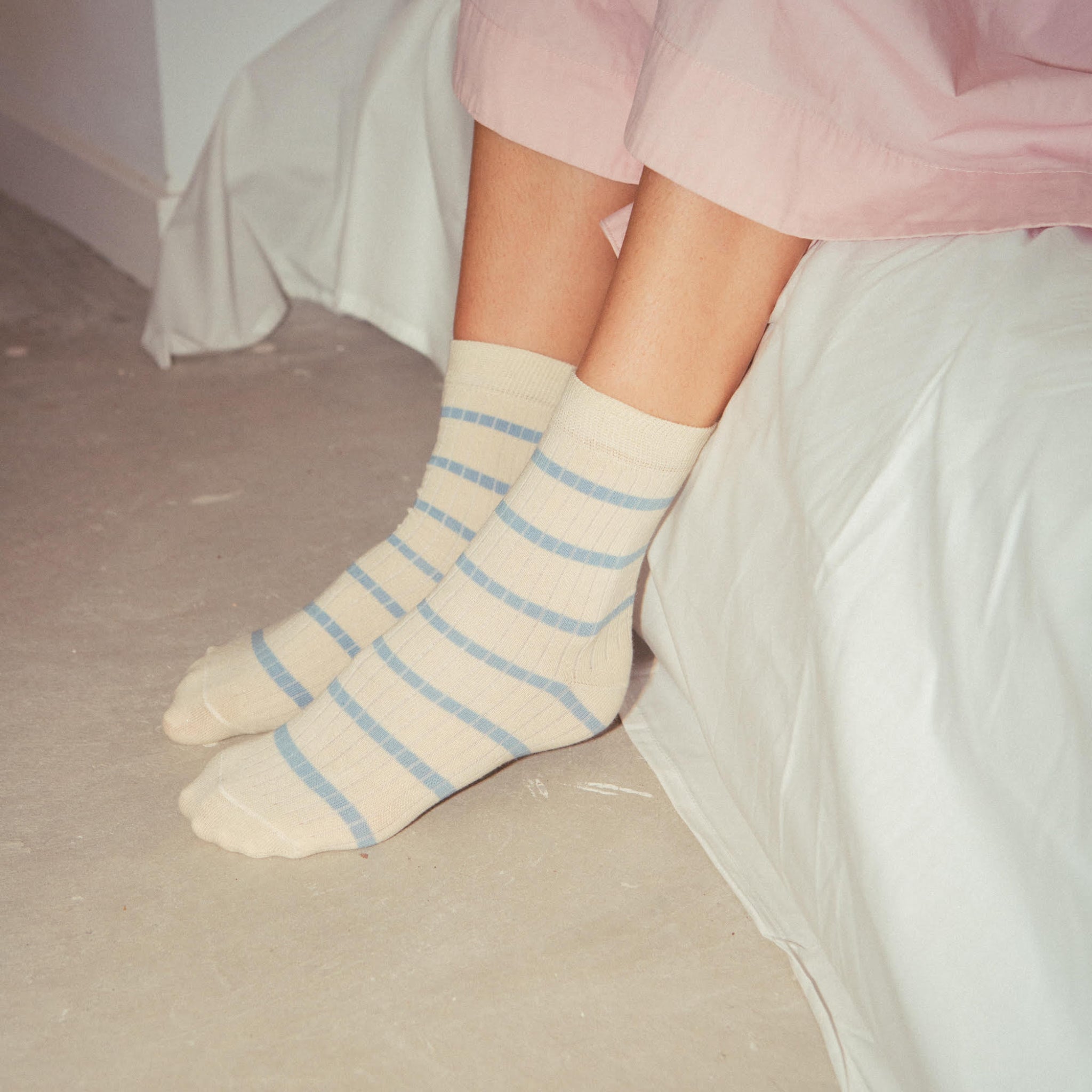 Person mit gestreiften Socken sitzt auf einem Bett mit weißer Bettwäsche.
