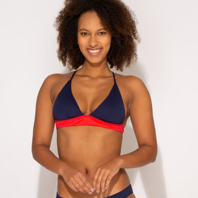 Frau mit lockigem Haar trägt einen zweifarbigen Bikini und lächelt in die Kamera vor weißem Hintergrund.