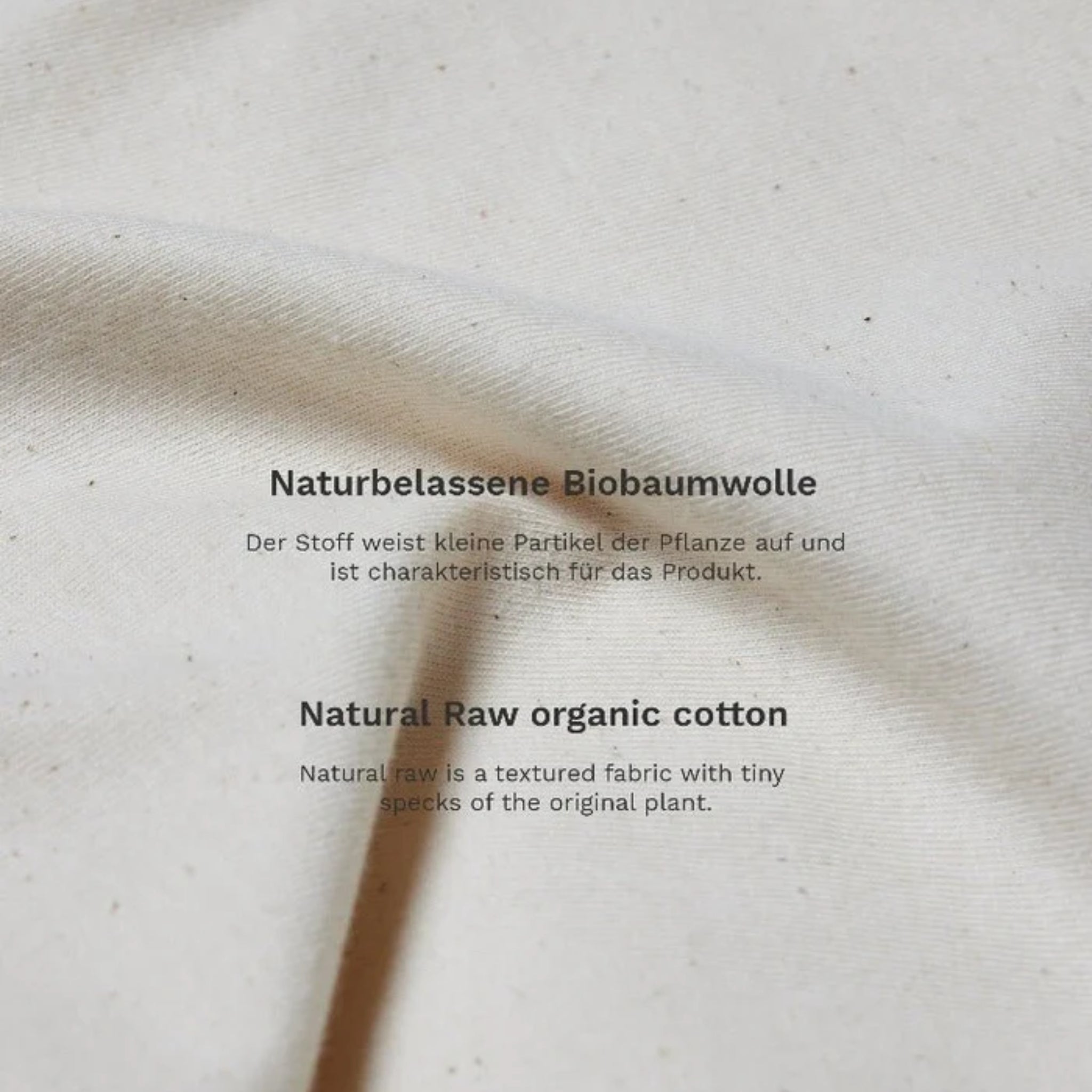 Beige Baumwollstoff mit Text über naturbelassene Bio-Baumwolle und kleine Pflanzenpartikel auf dem Material.
