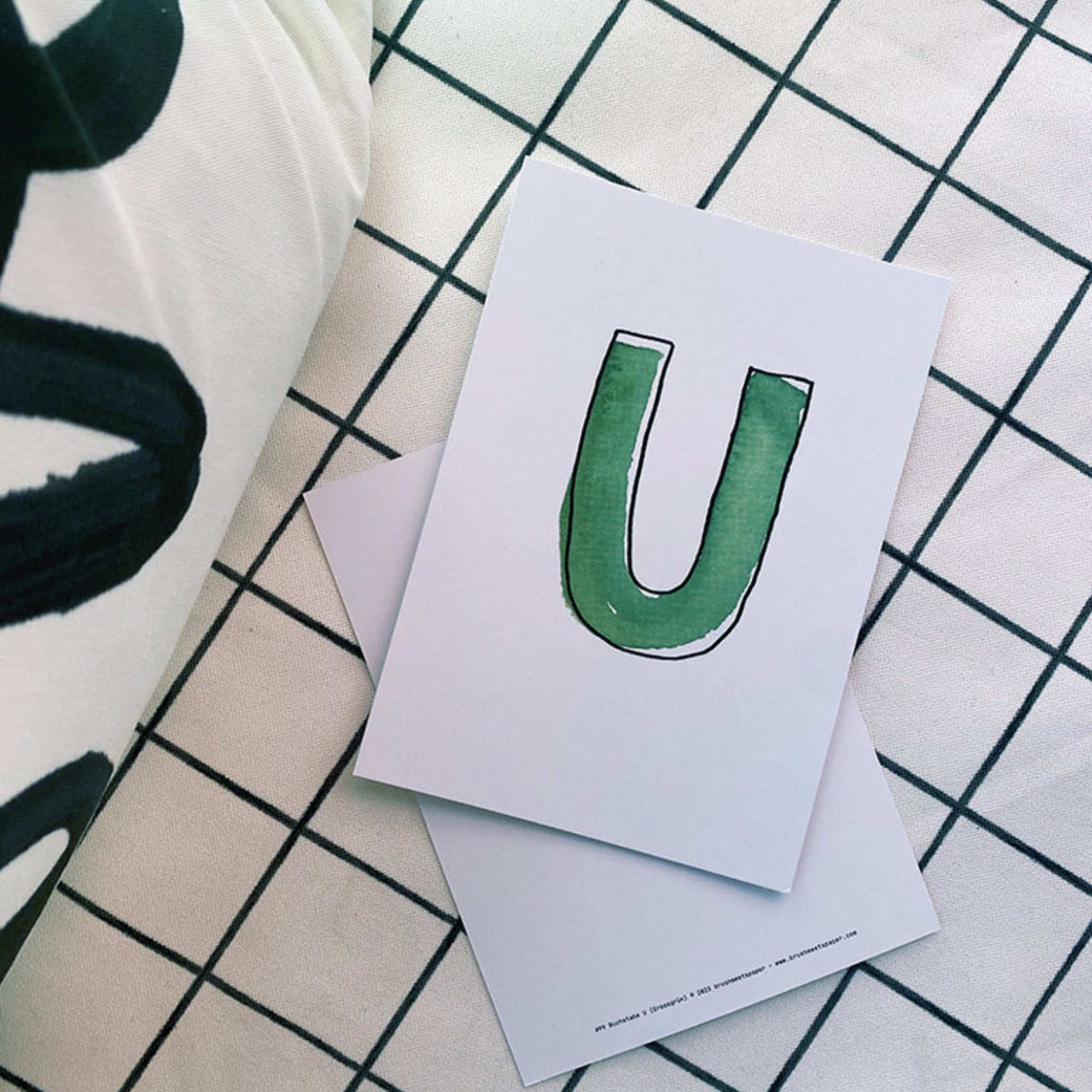 Weiße Karte mit grünem Buchstaben "U" auf einem karierten Untergrund.