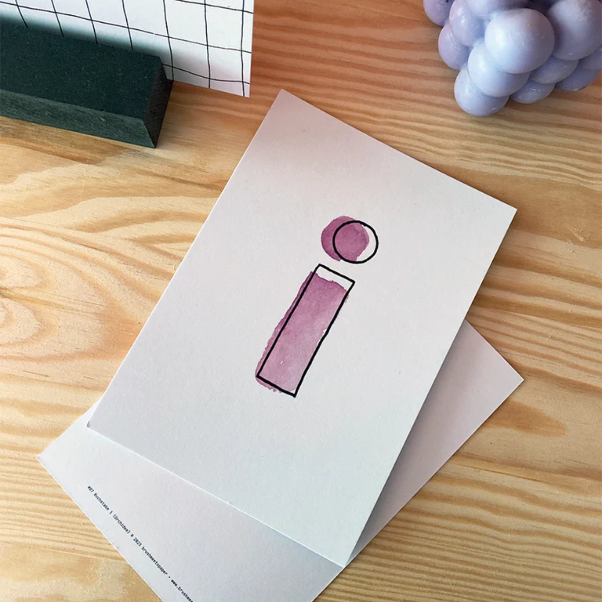 Zwei Karten auf einem Holztisch zeigen einen stilisierten Buchstaben "i" in Lila.