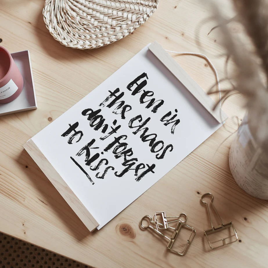 Tafel auf Holzuntergrund mit der Aufschrift: "Even in the chaos don't forget to kiss", daneben Büroklammern.