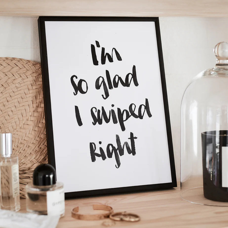 Gerahmtes Bild mit dem Text "I'm so glad I swiped right" auf einem Regal, umgeben von Parfümflaschen und Schmuck.
