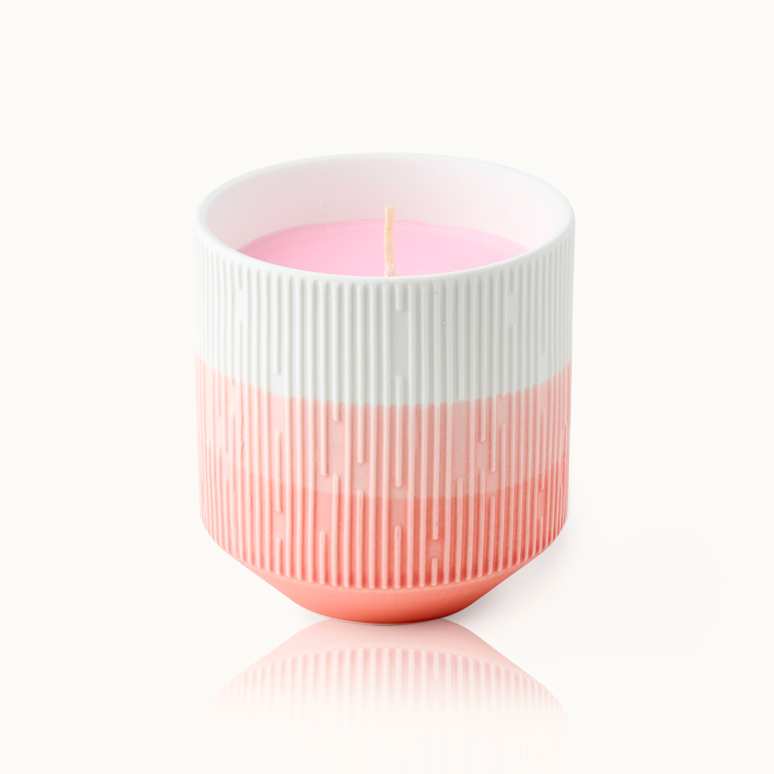 Weiße und orangefarbene geprägte Kerze in einem gestreiften Behälter mit einem Docht in der Mitte.