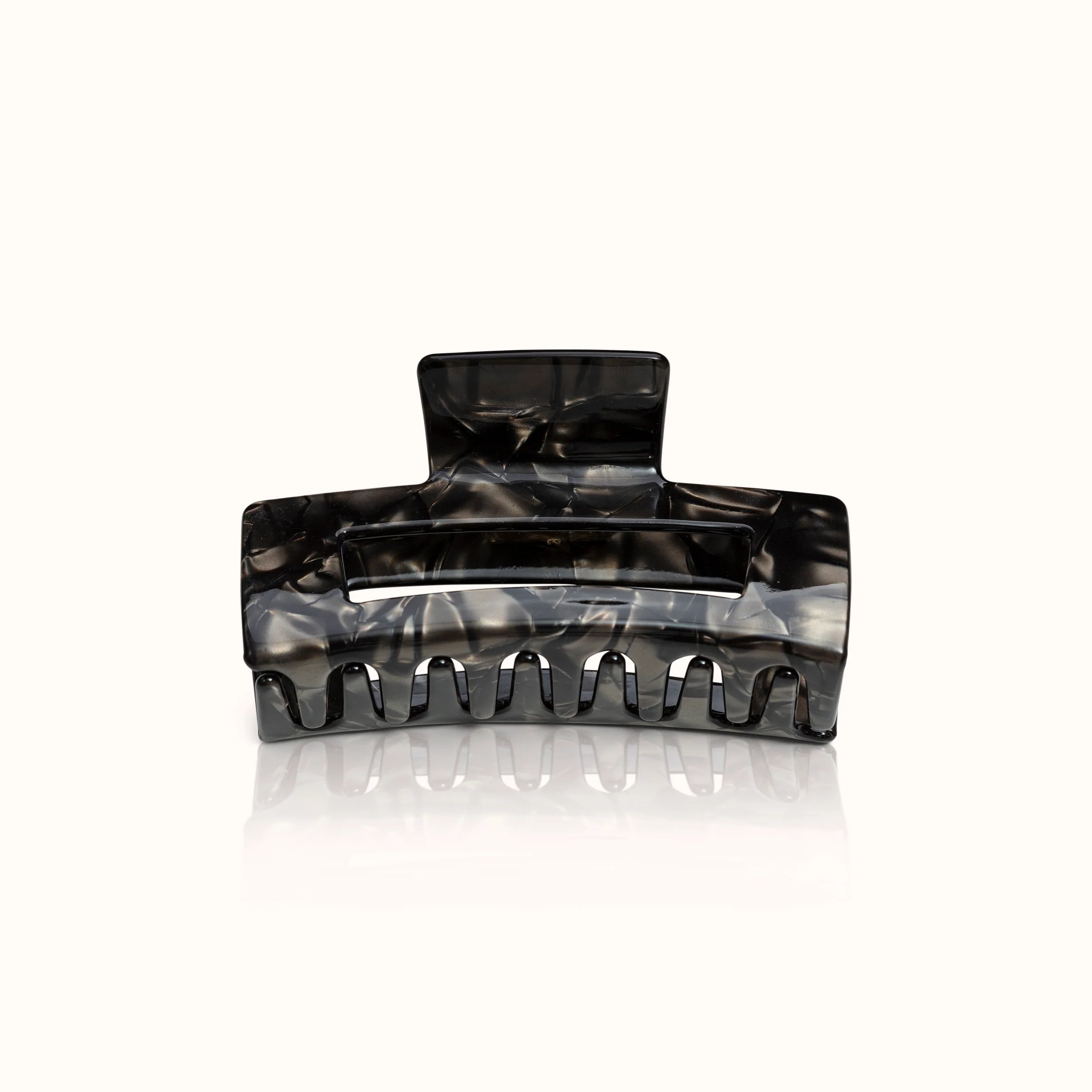 Schwarze Haarklammer vor hellem Hintergrund mit marmorierten Mustern und breiten Zähnen.