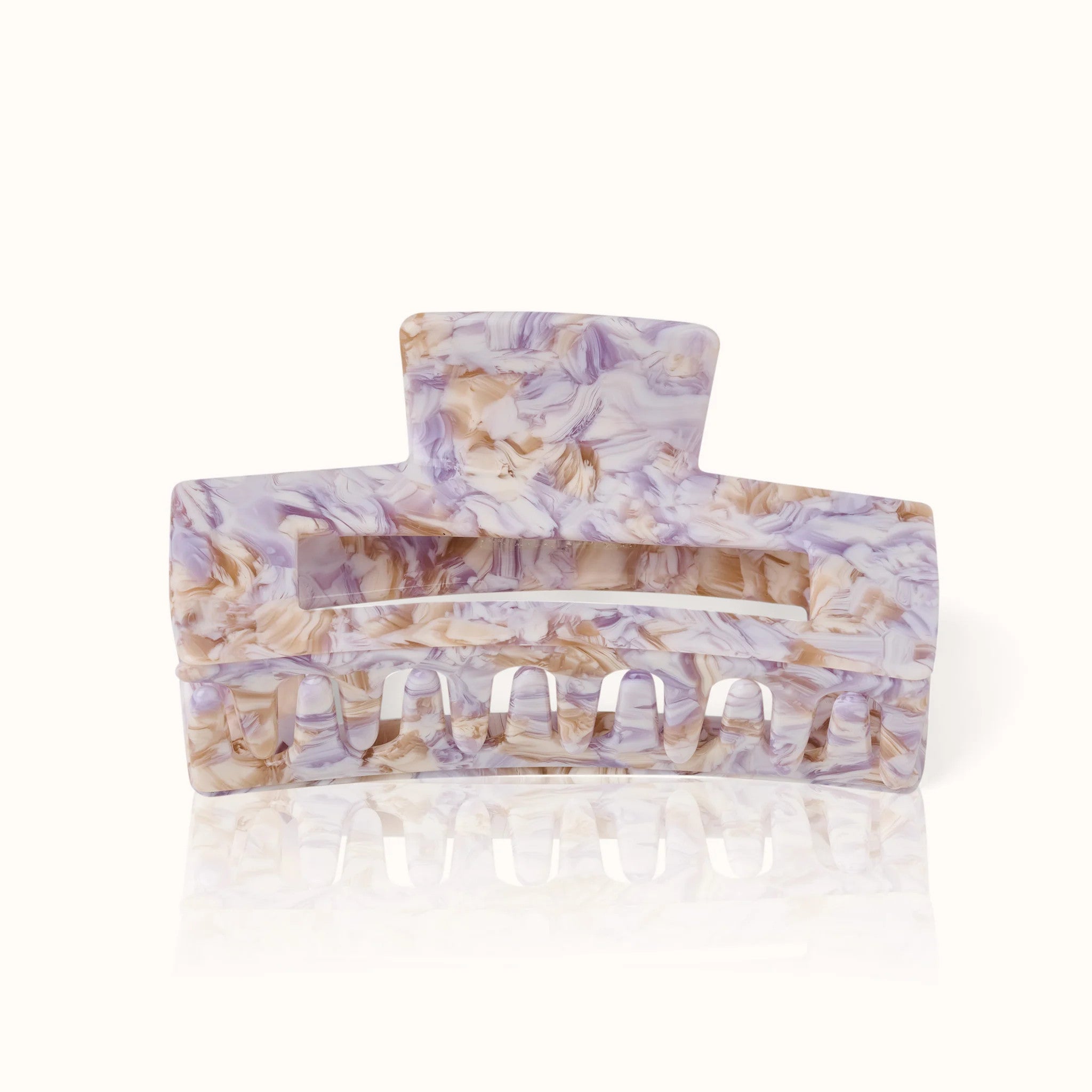 Lila-weiß-gemusterte Haarklammer mit breiten Zinken und breitem Griff, auf hellem Hintergrund.