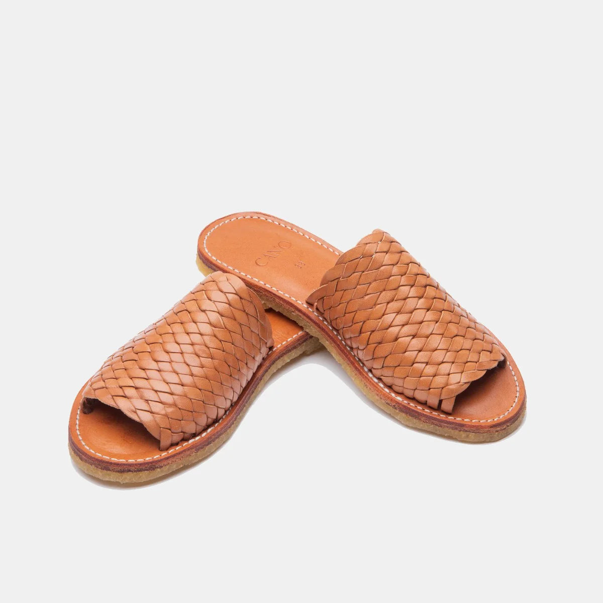 Ein Paar hellbraune Ledersandalen mit gewebtem Obermaterial und flacher Sohle auf einem schlichten weißen Hintergrund.