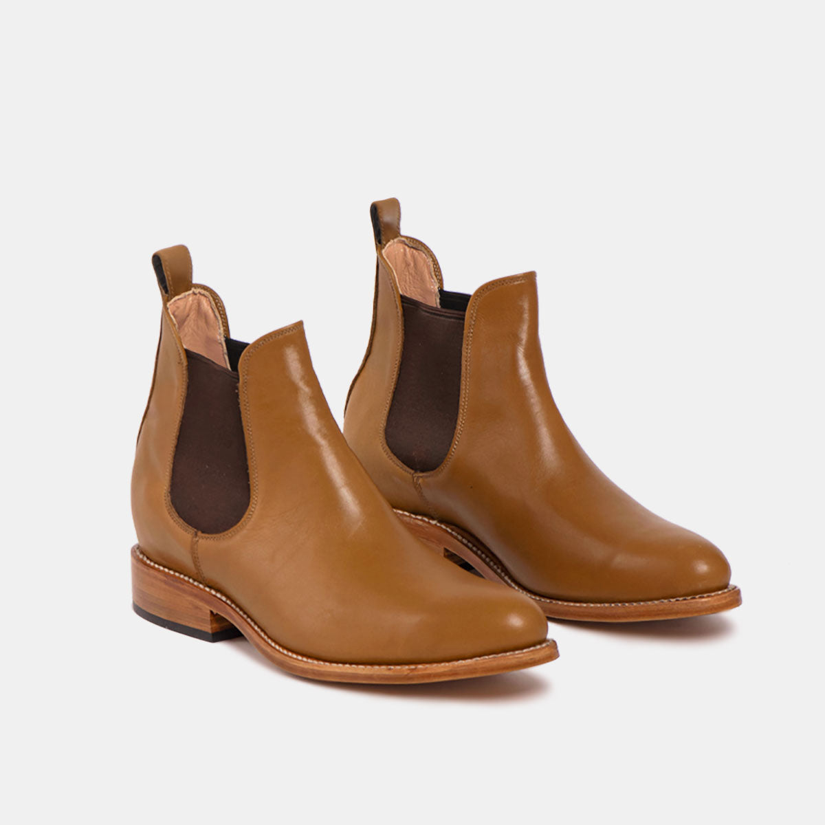 Ein Paar braune Chelsea-Stiefel aus Leder mit elastischen Seitenteilen, Zuglaschen an der Rückseite und niedrigen Holzabsätzen, die vor einem weißen Hintergrund gezeigt werden.