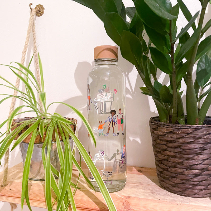 Glasflasche mit bunten Illustrationen, umgeben von Zimmerpflanzen auf einem Holzregal.