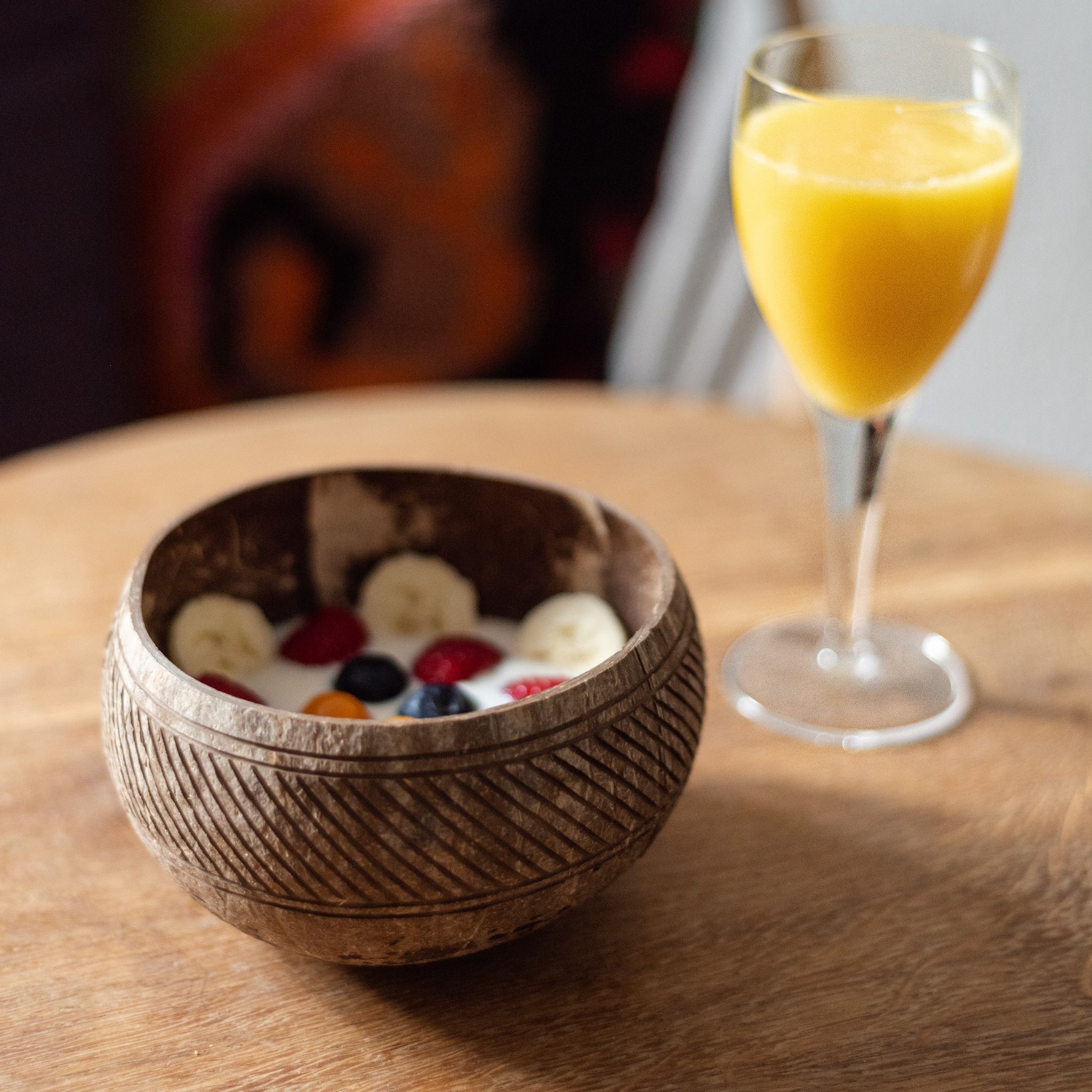 Holzschale mit Joghurt, Bananenscheiben und Beeren neben einem Glas mit Orangensaft auf einem Holztisch.