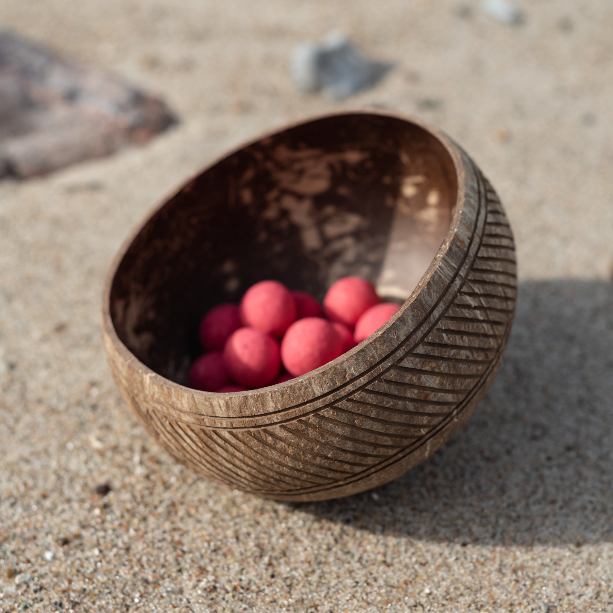 Holzschale mit rosa Kugeln auf Sand.