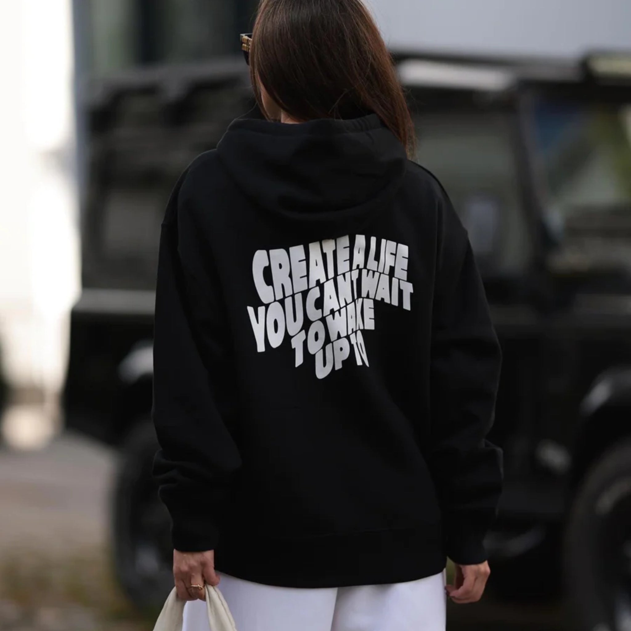 Frau von hinten mit schwarzem Hoodie, darauf der Text "CREATE A LIFE YOU CAN'T WAIT TO WAKE UP TO" in Weiß.