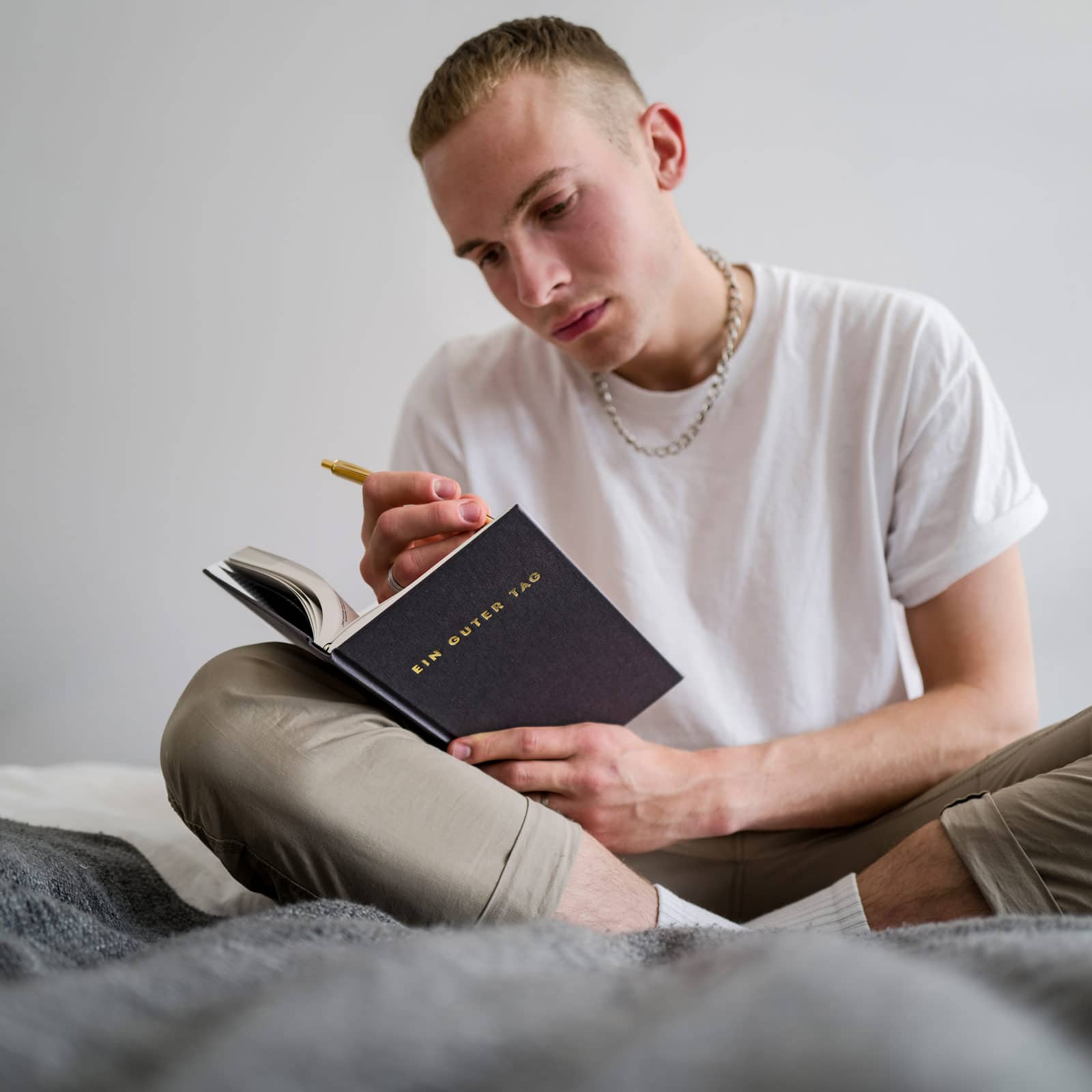Eine Person in weißem T-Shirt sitzt und schreibt in ein schwarzes Notizbuch mit der Aufschrift "EIN GUTER TAG".