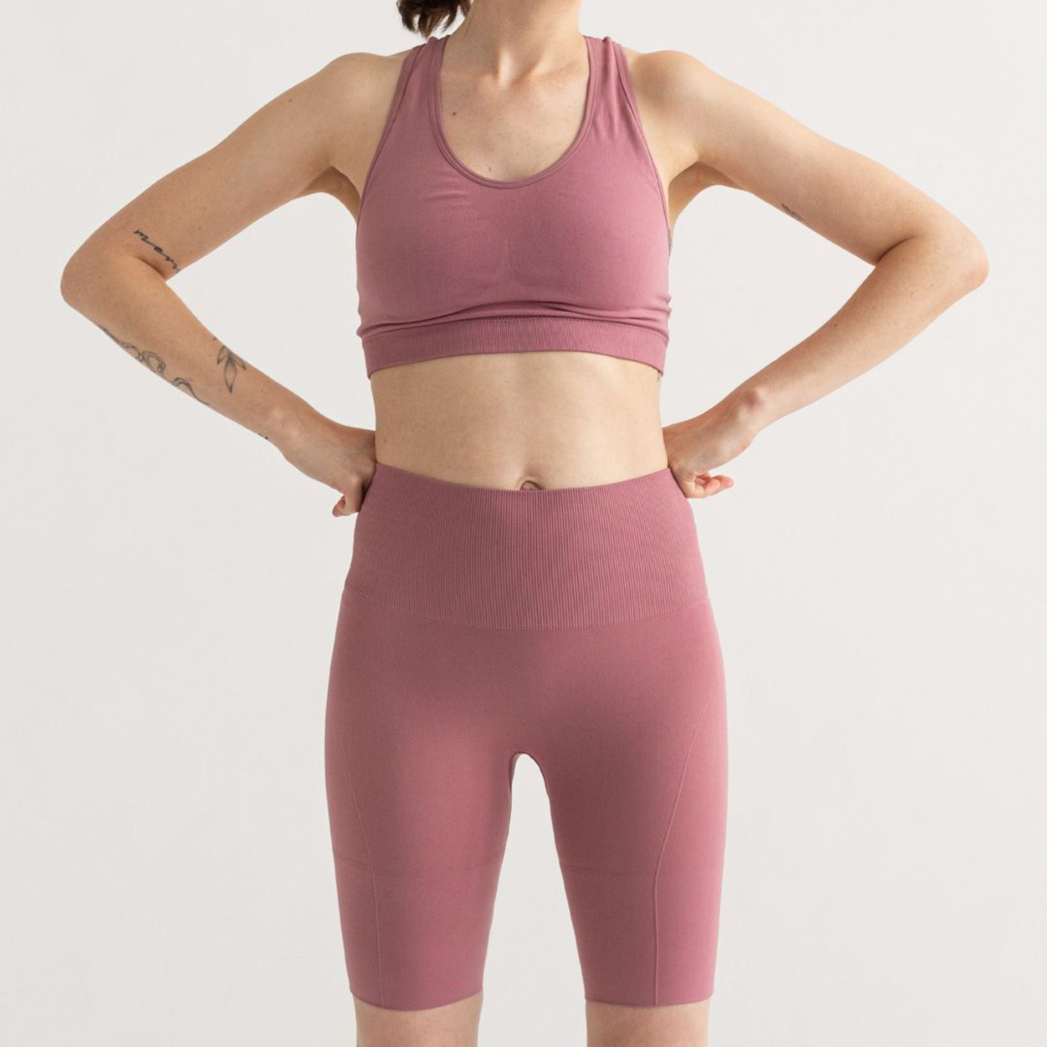 Person in pink athletic wear poses with hands on hips against a plain background.