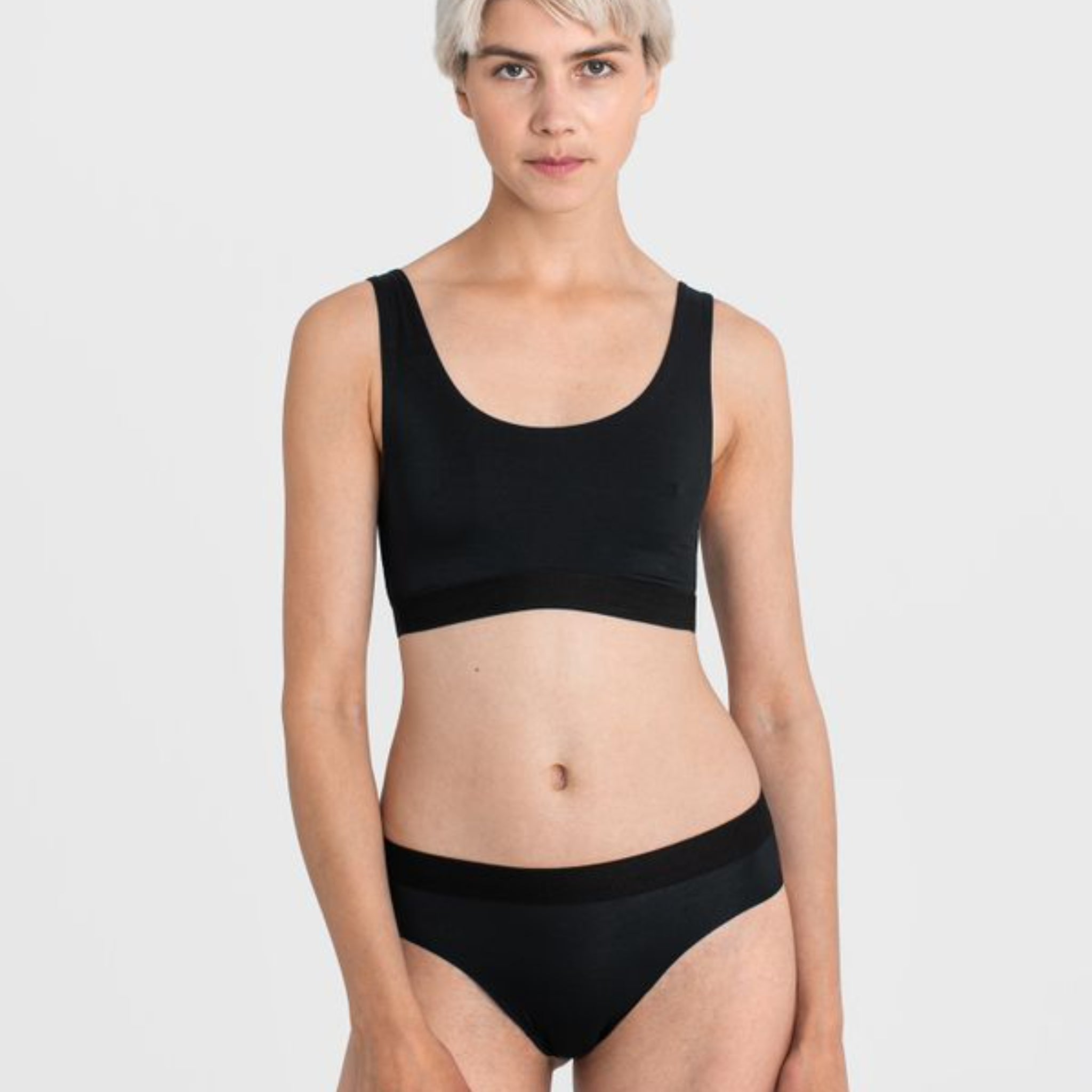 Person in schwarzer Unterwäsche vor grauem Hintergrund.