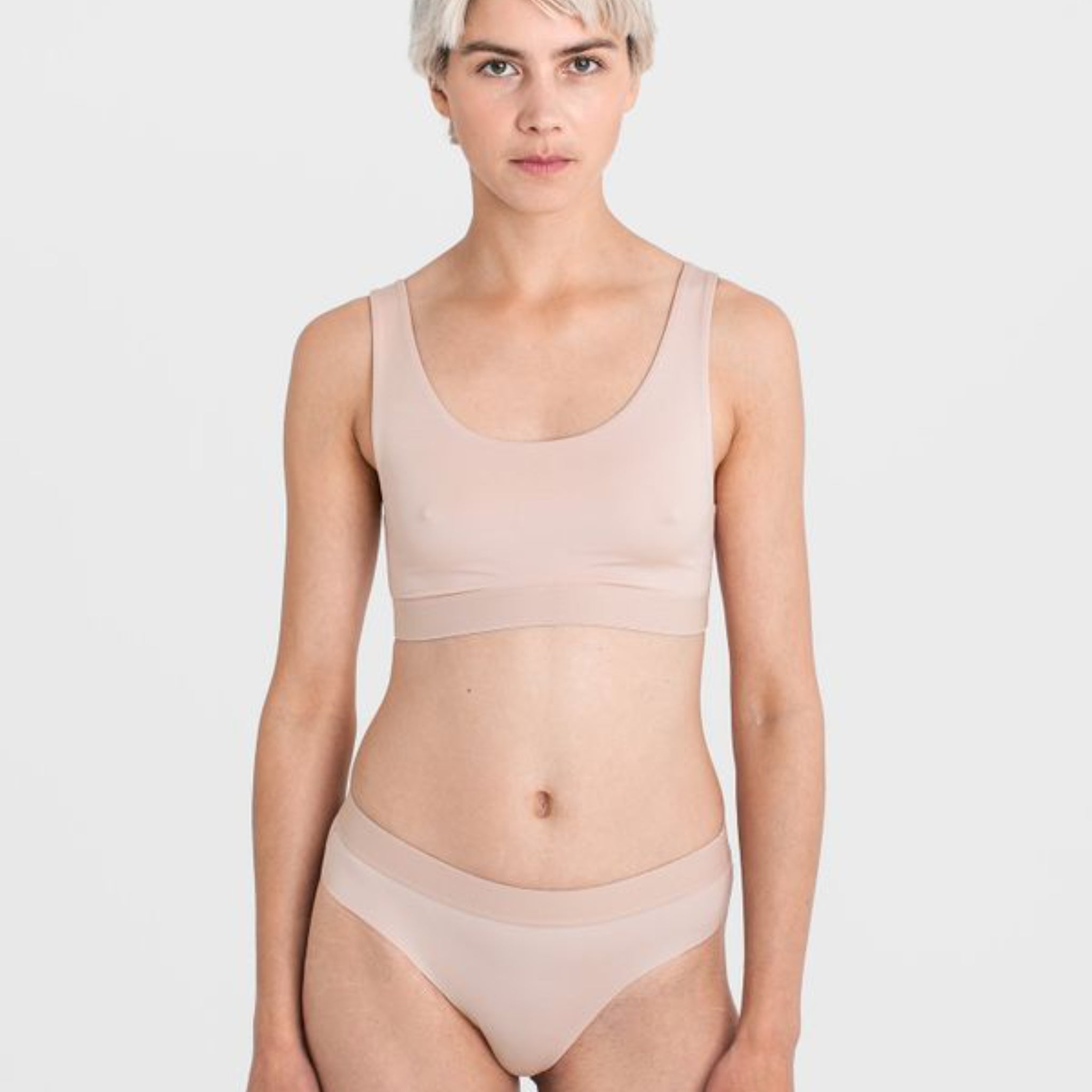 Person in beige Unterwäsche vor neutralem Hintergrund.