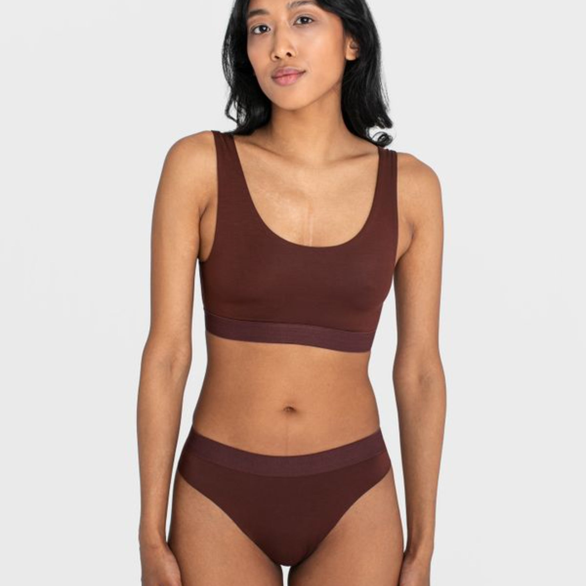 Frau in braunem Sport-BH und Unterhose vor neutralem Hintergrund.