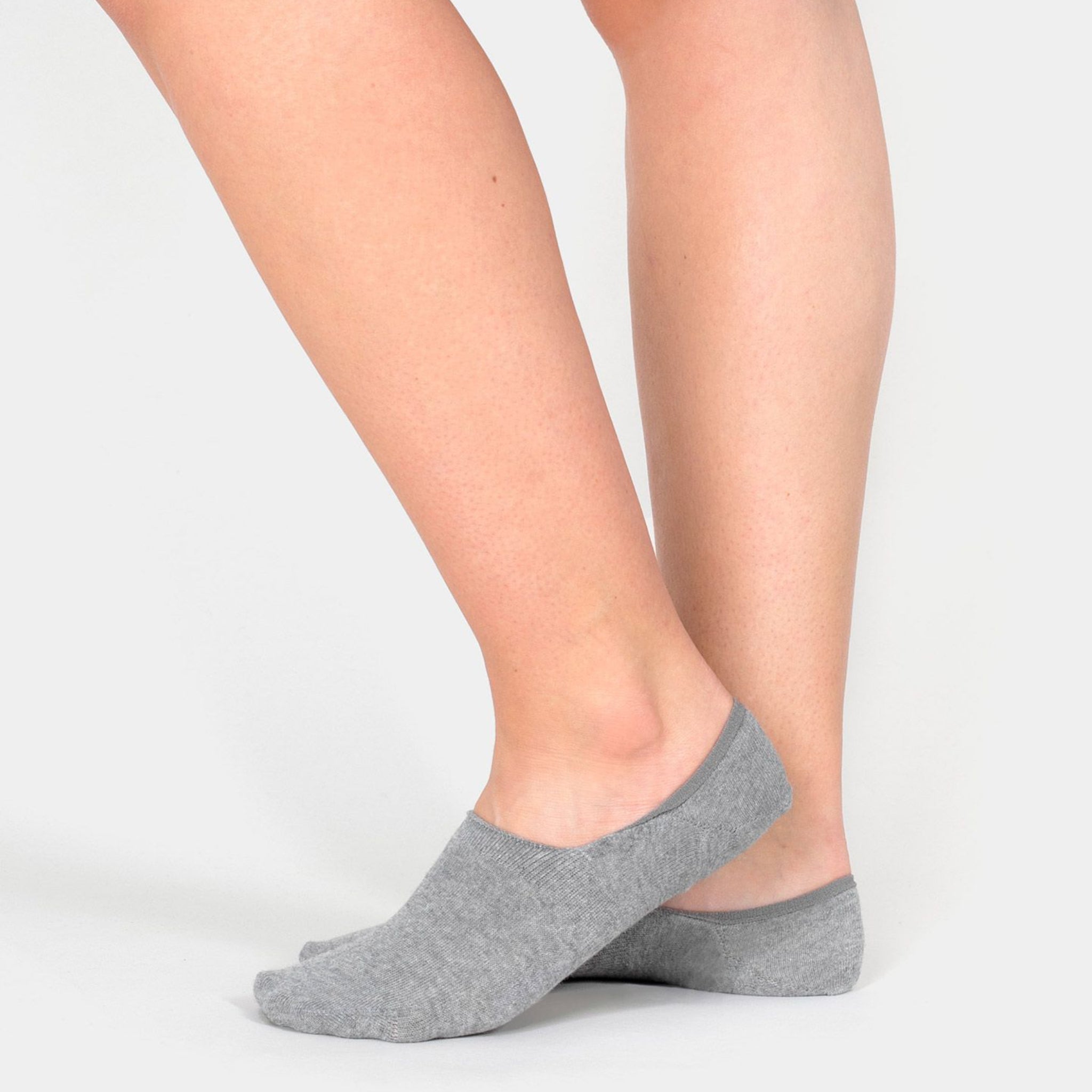Person trägt graue No-Show-Socken auf nackten Füßen vor einem weißen Hintergrund.
