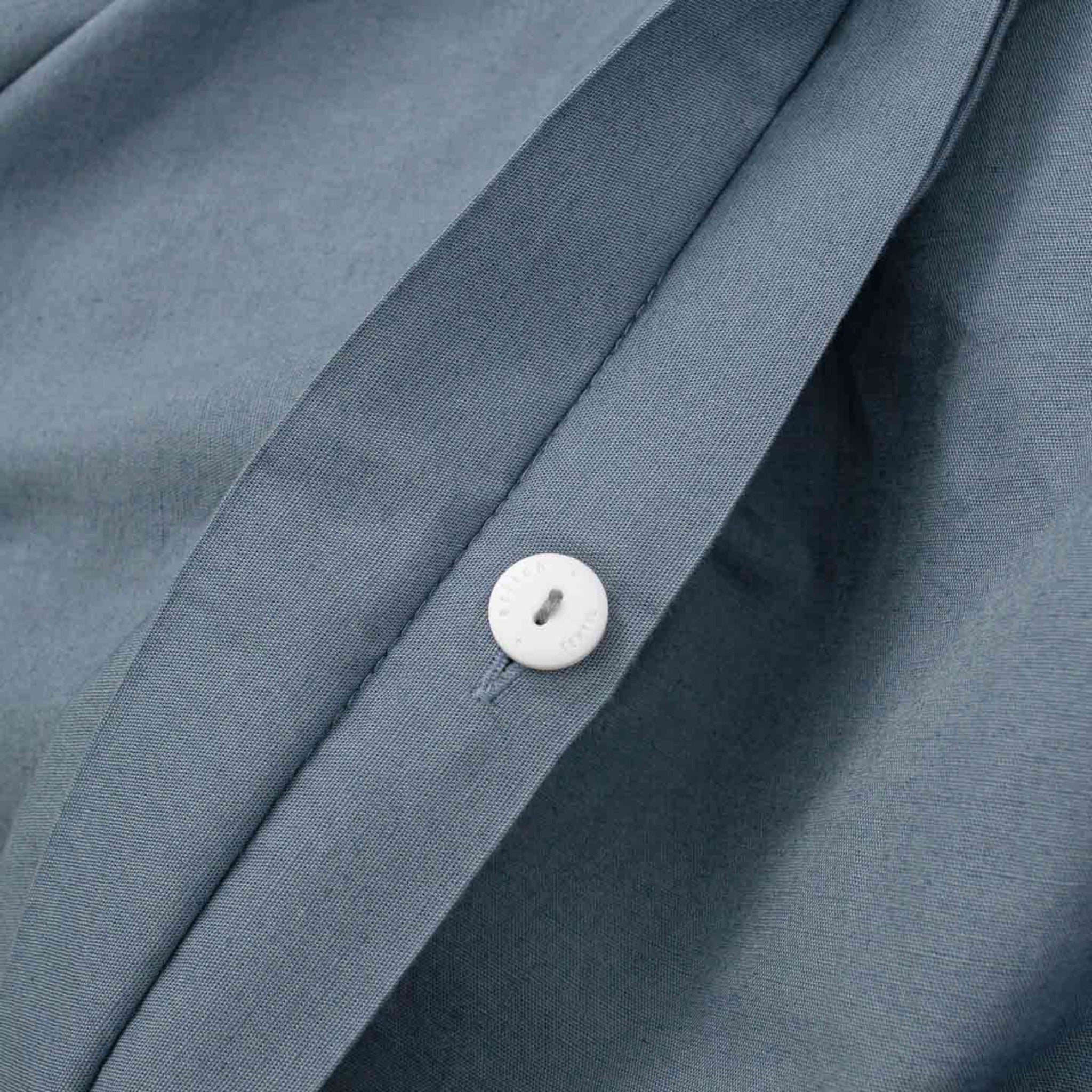 Nahaufnahme eines grauen Hemdes mit einem weißen Knopf an der Knopfleiste.