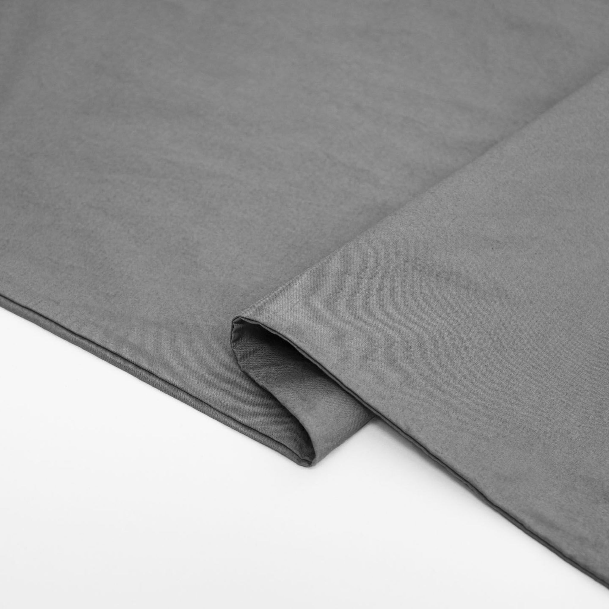 Graues Stoffstück, das auf einer hellen Oberfläche liegt, mit einer Ecke leicht gefaltet.