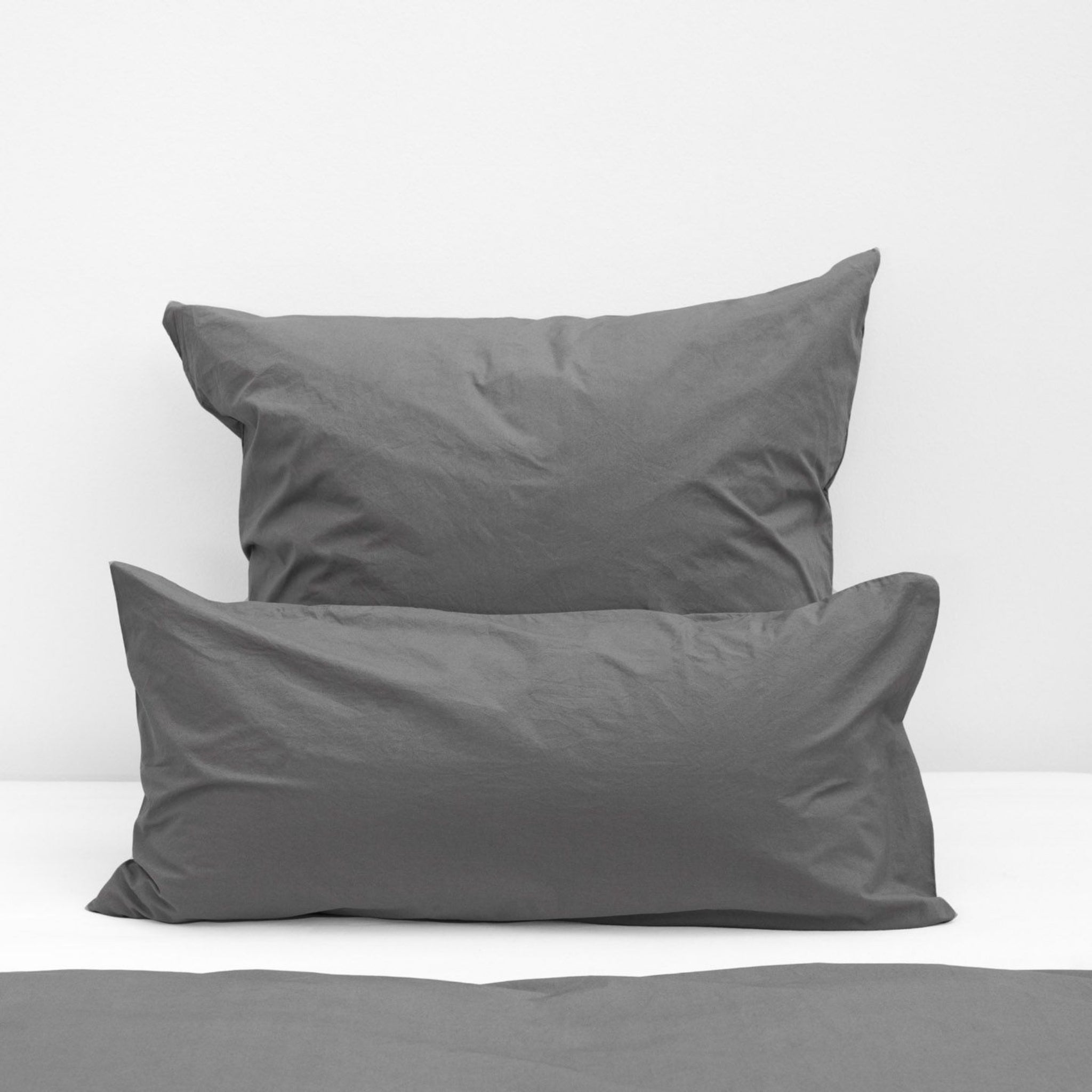 Zwei graue Kissen auf einem weißen Bett.