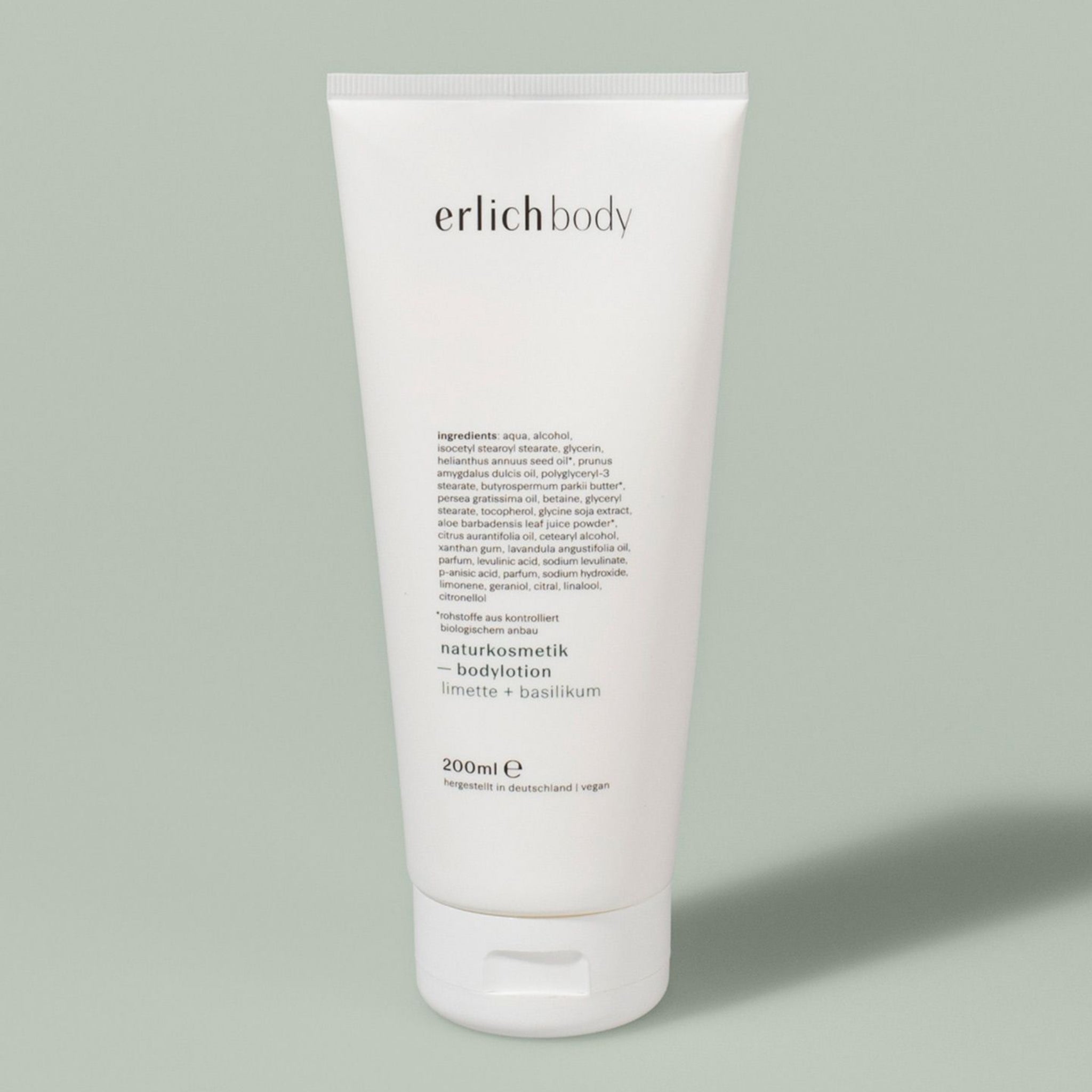 Weiße Tube der erlich body Naturkosmetik Bodylotion mit Limette und Basilikum auf grauem Hintergrund.