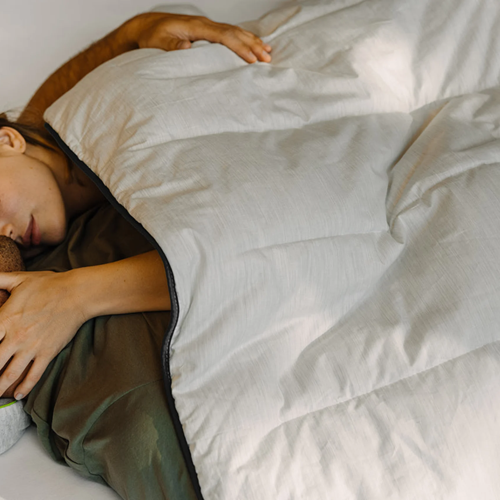 Zwei Personen liegen eng nebeneinander unter einer cremefarbenen Decke.