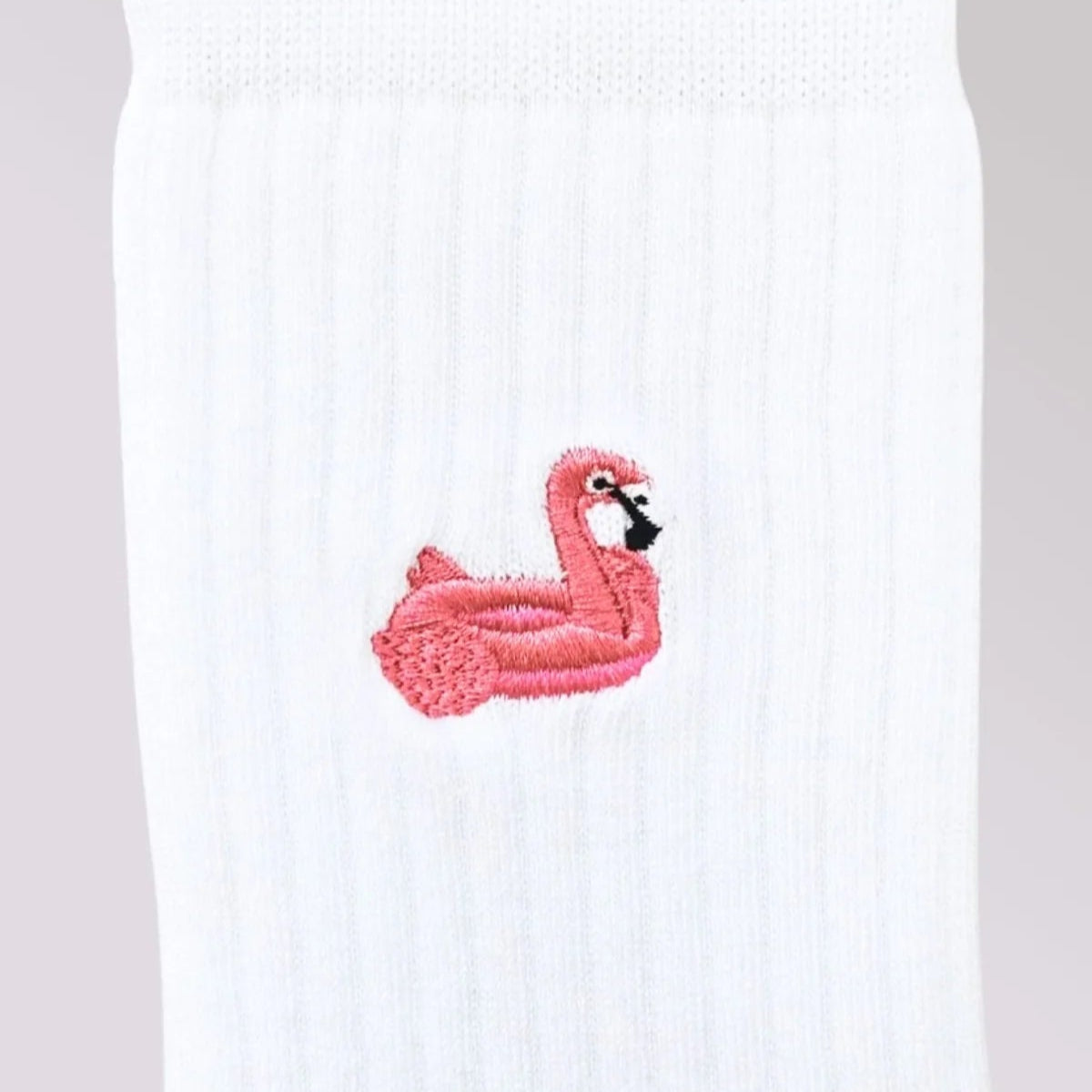 Nahaufnahme einer weißen gerippten Socke mit einem aufgestickten rosa aufblasbaren Flamingo-Schwimmer mit schwarzem Schnabel und weißem Gesicht.