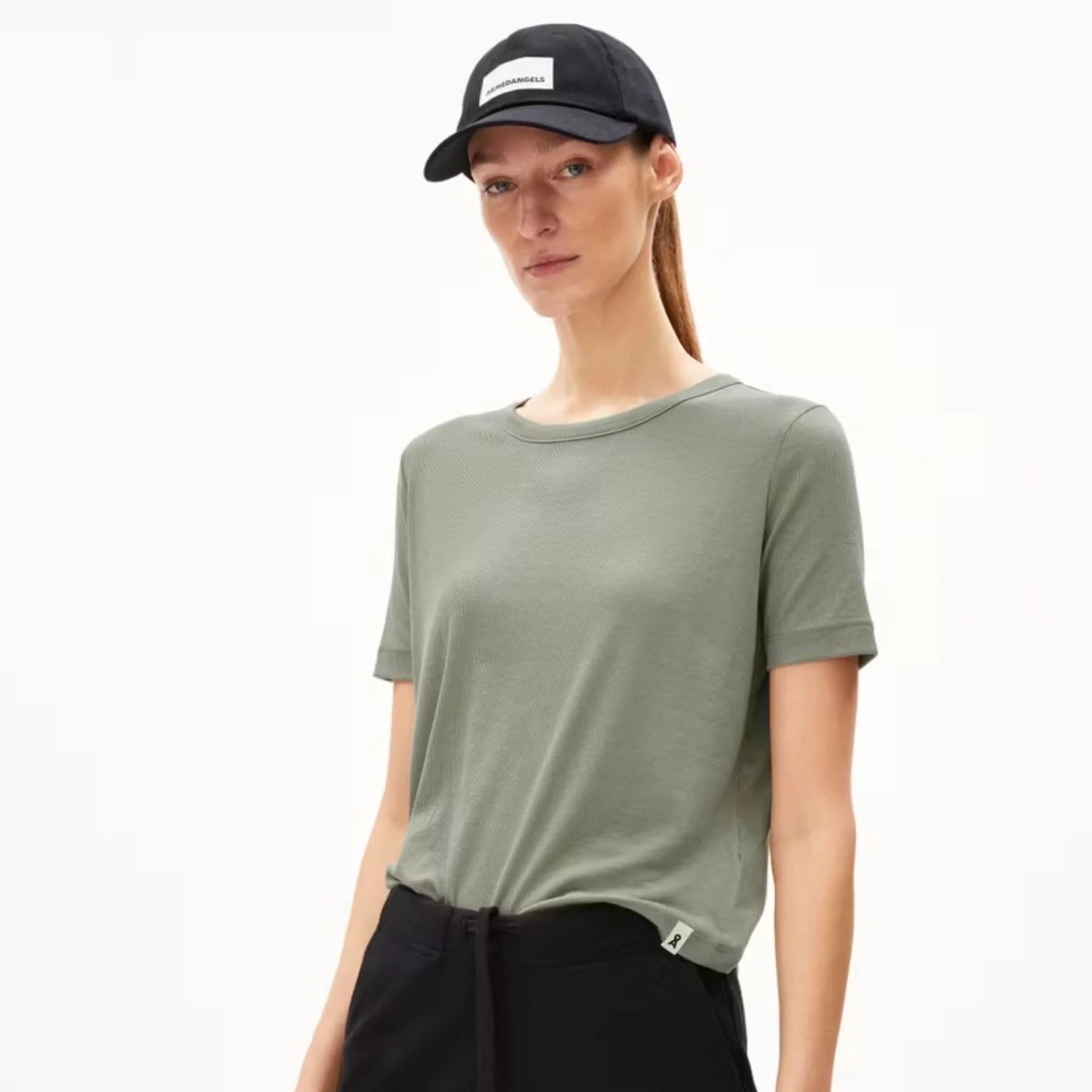 Eine Person, die ein hellgrünes, kurzärmeliges T-Shirt, eine schwarze Hose und eine schwarze Baseballmütze trägt, steht vor einem schlichten weißen Hintergrund.