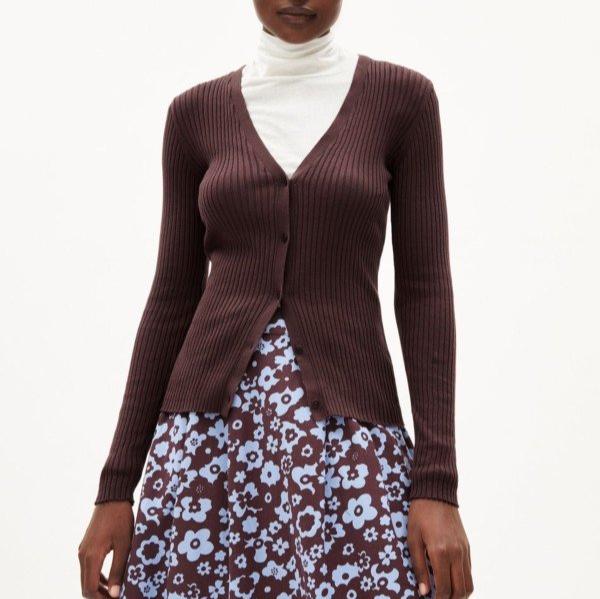 Person trägt einen braunen Strickpullover über einem weißen Oberteil und einen Rock mit blau-braunem Blumenmuster.