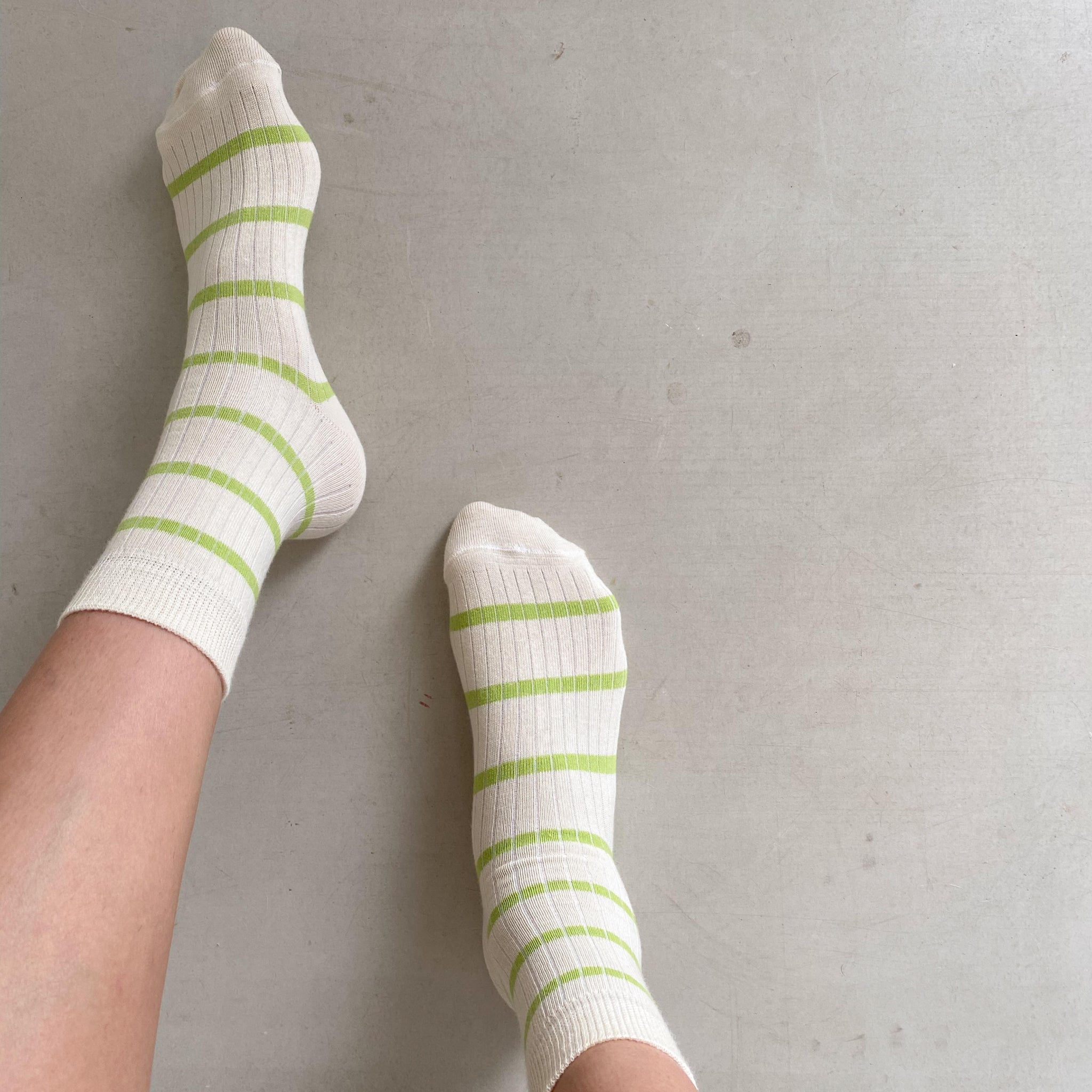 Zwei Füße in weißen Socken mit grünen Streifen auf einem hellen, strukturierten Boden.