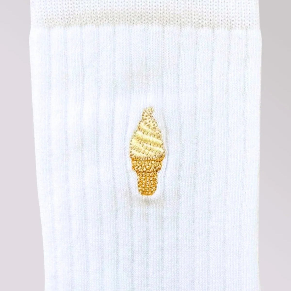 Eine weiße gerippte Socke mit einem kleinen gestickten gelben Eistütenmuster in der Mitte.