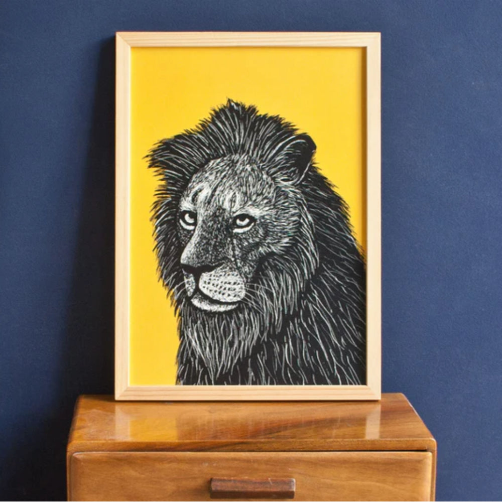 Eine gerahmte Schwarz-Weiß-Illustration eines Löwen mit großer Mähne vor einem leuchtend gelben Hintergrund befindet sich auf einem hölzernen Schubladenschrank vor einer dunkelblauen Wand.