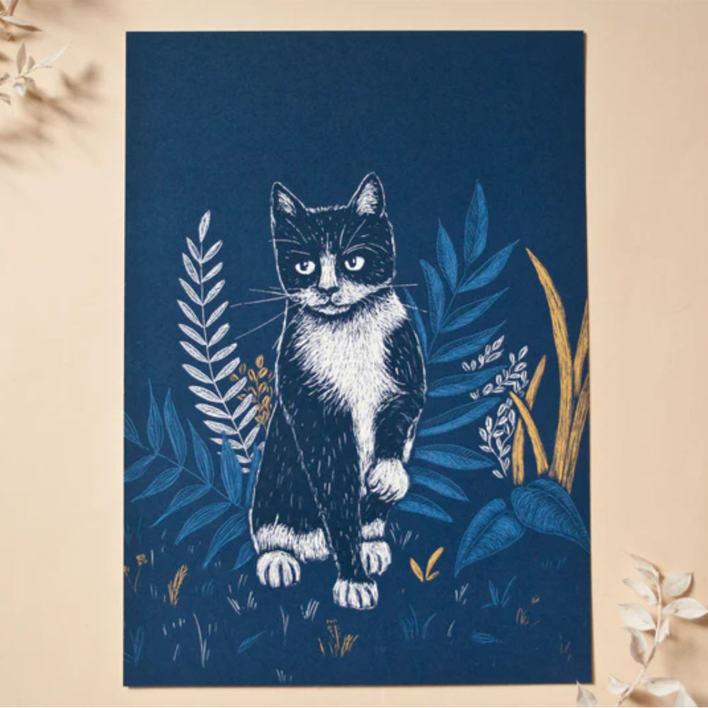 Die Zeichnung einer schwarz-weißen Katze mit ernstem Gesichtsausdruck sitzt inmitten illustrierter blauer und gelber Pflanzen auf dunkelblauem Hintergrund. Das Kunstwerk befindet sich auf einer beigen Fläche mit einigen getrockneten Blättern in der Nähe.