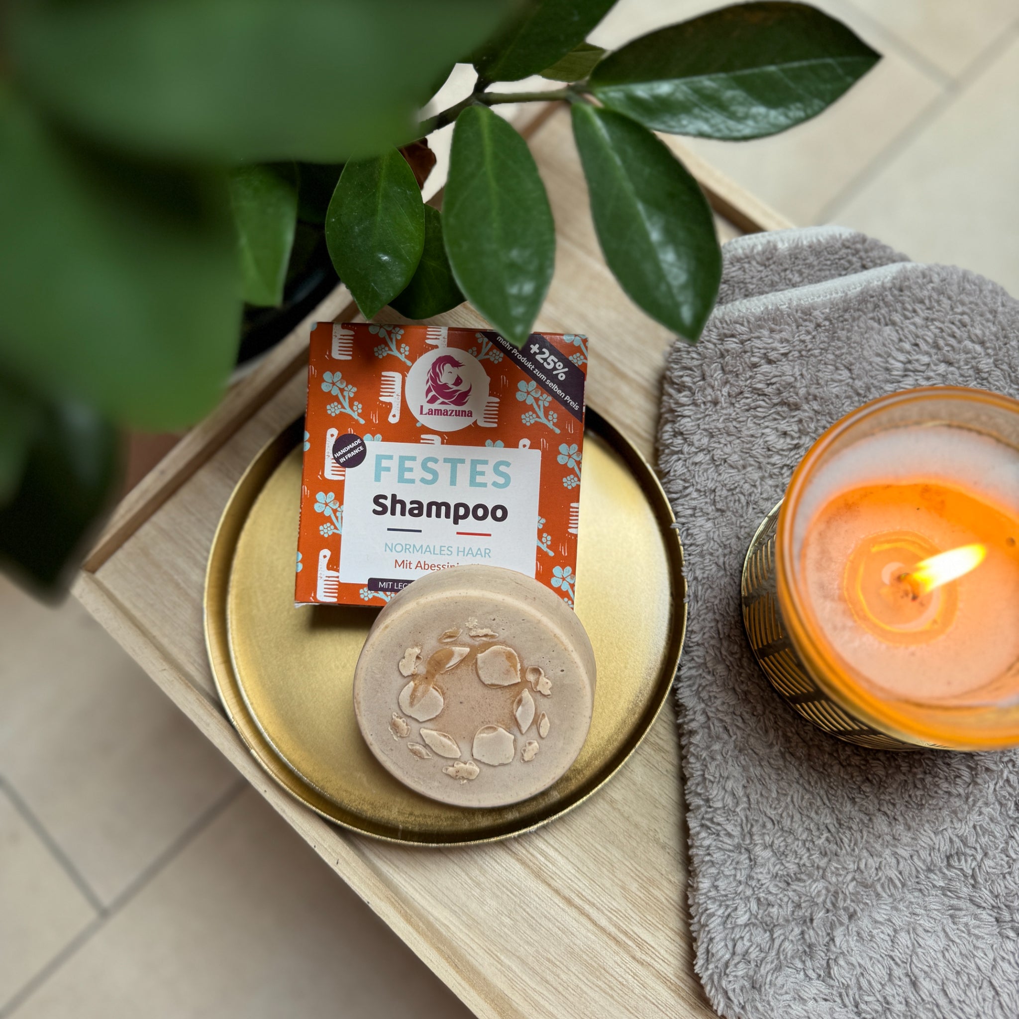 Festes Shampoo auf einem goldenen Teller neben einer brennenden Kerze und einer Pflanze.