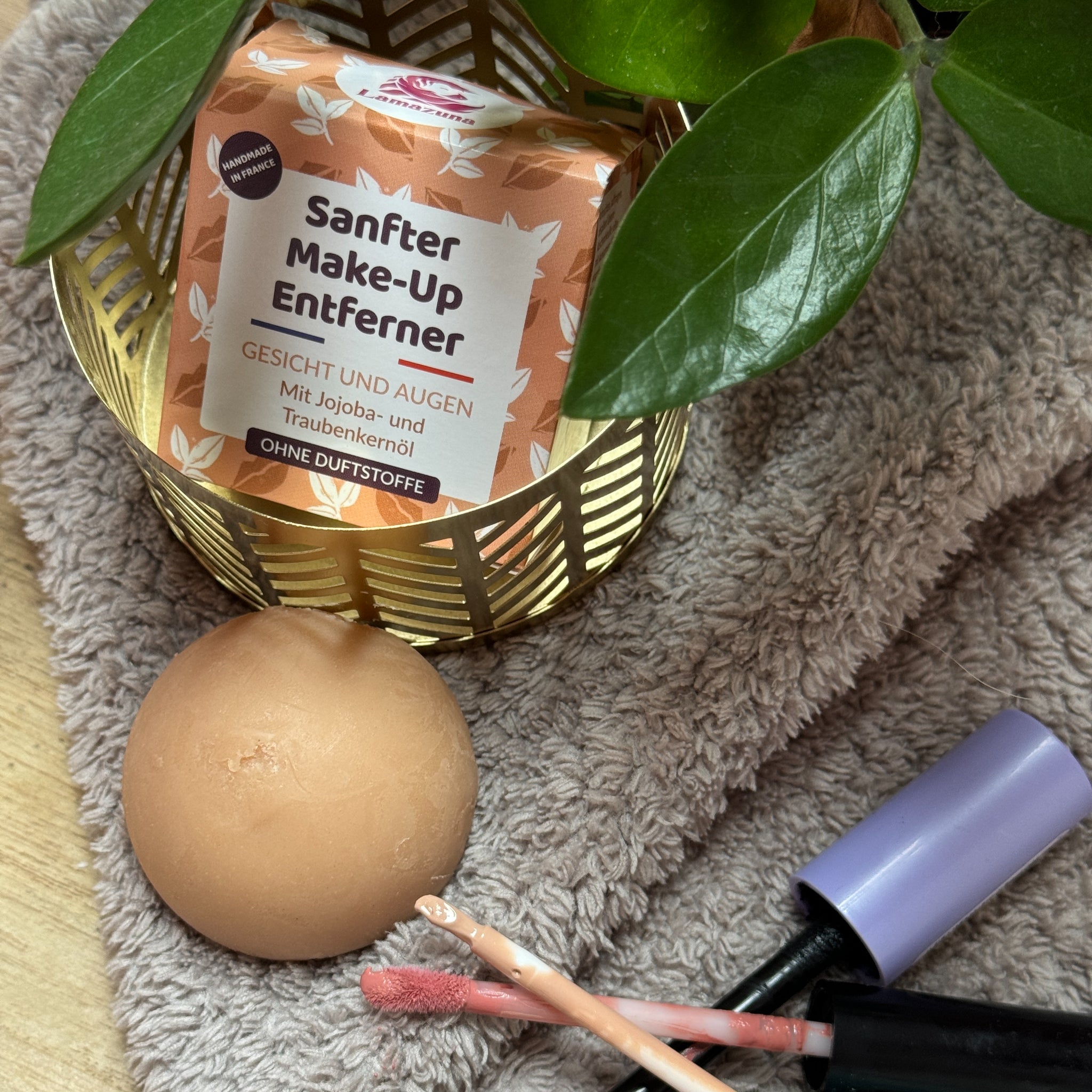 Kosmetikprodukte auf einem Handtuch: Make-up-Entferner, ein runder Schwamm, Make-up-Stift und Pflanzenblätter.