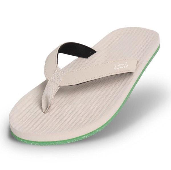 Beiger Flip-Flop mit strukturiertem Fußbett und grüner Sohle, schwebend vor weißem Hintergrund.